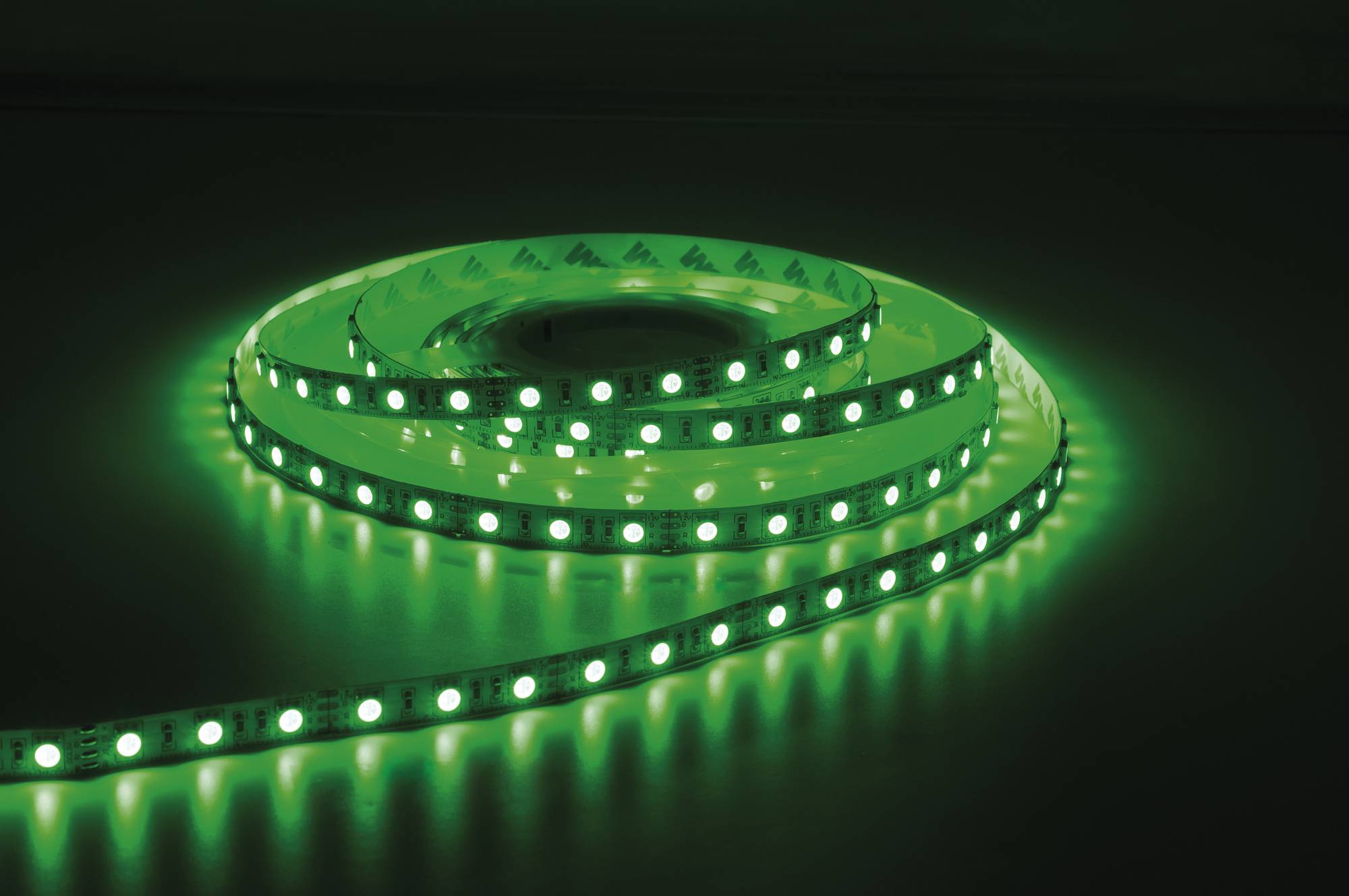Ein leuchtender grüner LED-Streifenlichter ist auf einer dunklen Oberfläche aufgewickelt und beleuchtet die Umgebung mit einem hellen, lebendigen Grünton.
