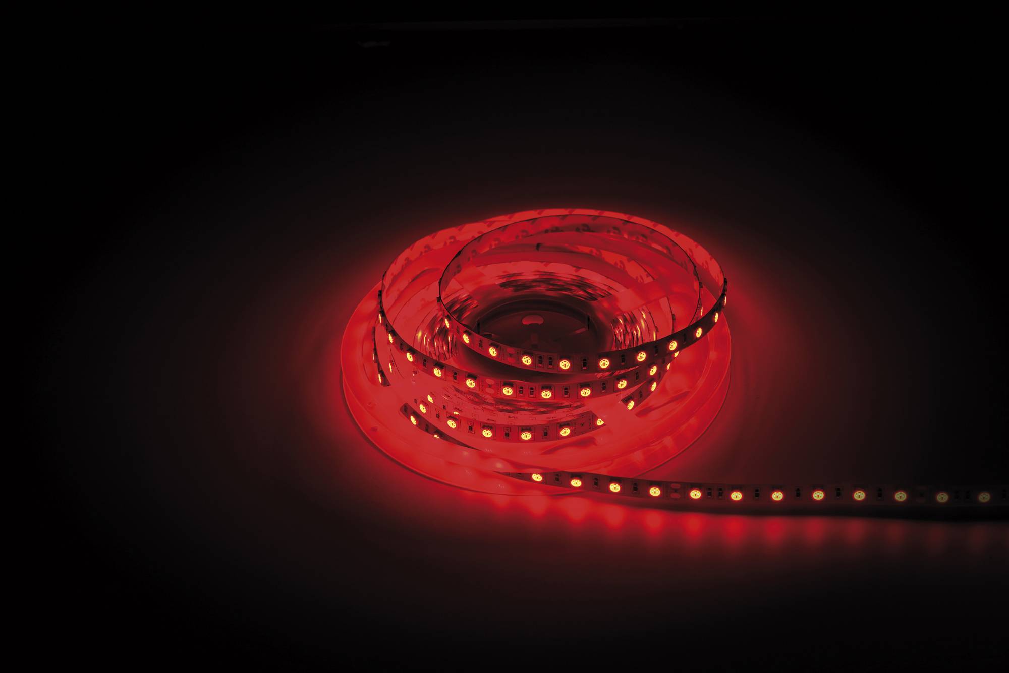 Ein aufgerolltes rotes LED-Lichtband gibt ein weiches Licht gegen einen dunklen Hintergrund ab und zeigt seine Flexibilität und Leuchtkraft.