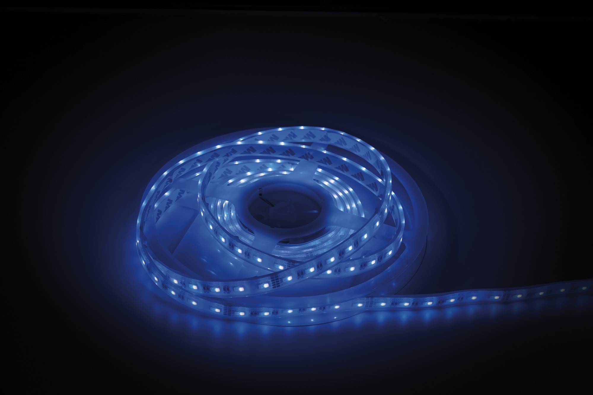Ein leuchtender blauer LED-Streifenleuchte, die auf einer dunklen Oberfläche aufgerollt ist und ihre Umgebung mit einem sanften blauen Farbton beleuchtet.
