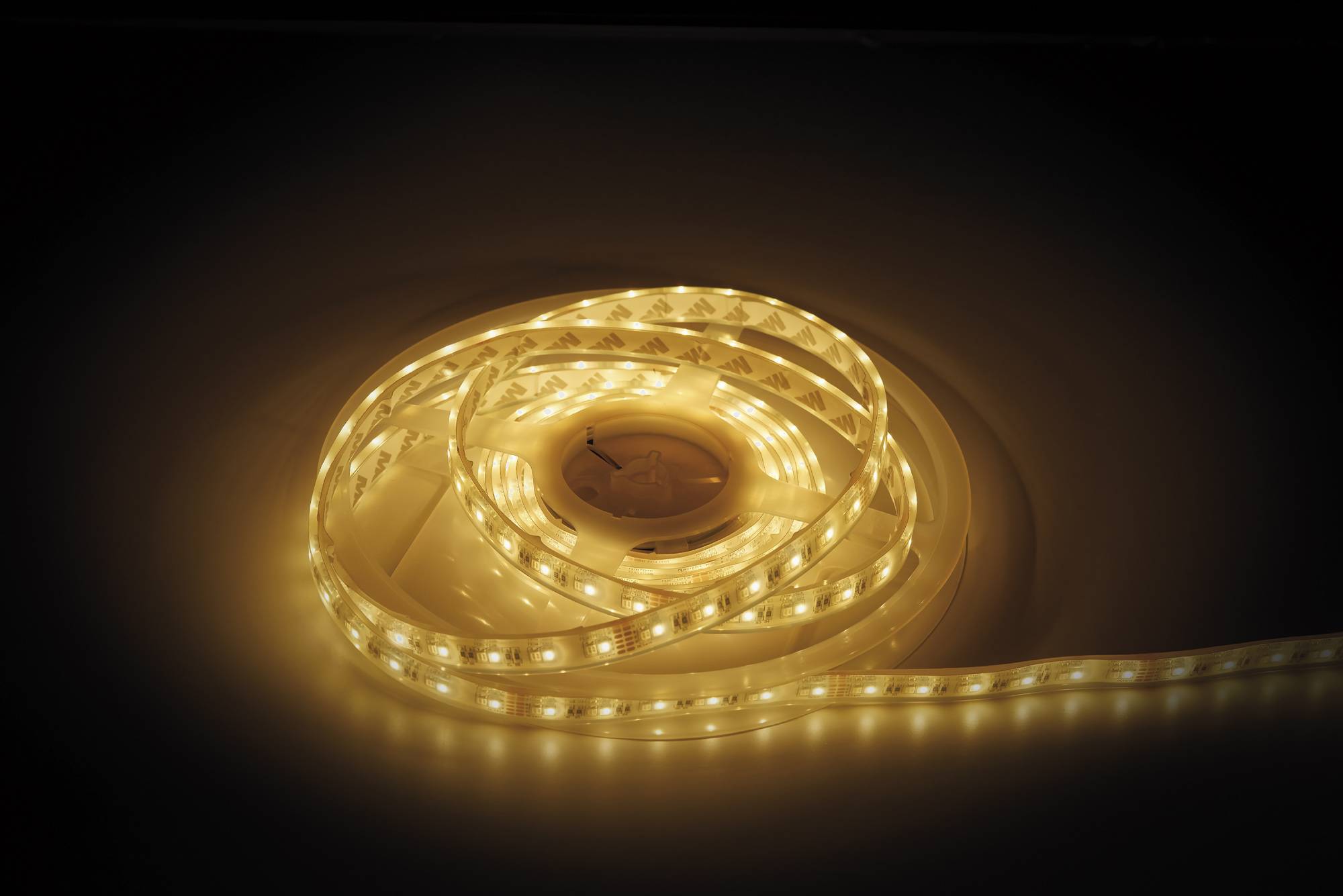 Ein aufgerollter Streifen aus warmweißen LED-Leuchten, die auf einer dunklen Oberfläche leuchten und eine sanfte und stimmungsvolle Beleuchtung erzeugen.