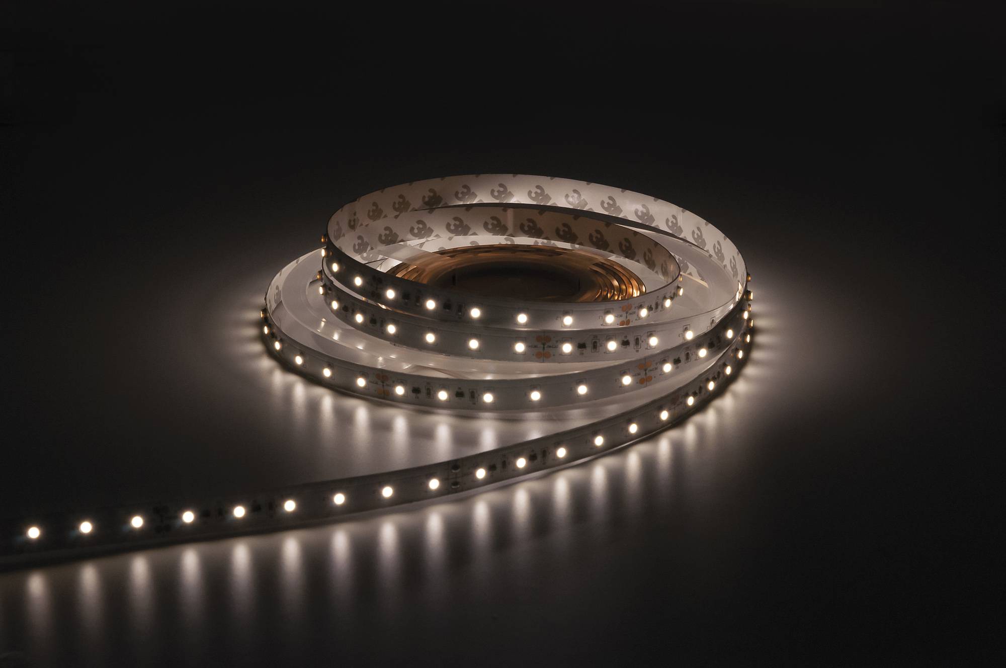 Ein aufgerollter LED-Lichtstreifen erzeugt ein warmes Glühen in einer dunklen Umgebung und schafft eine Spirale aus Beleuchtung.