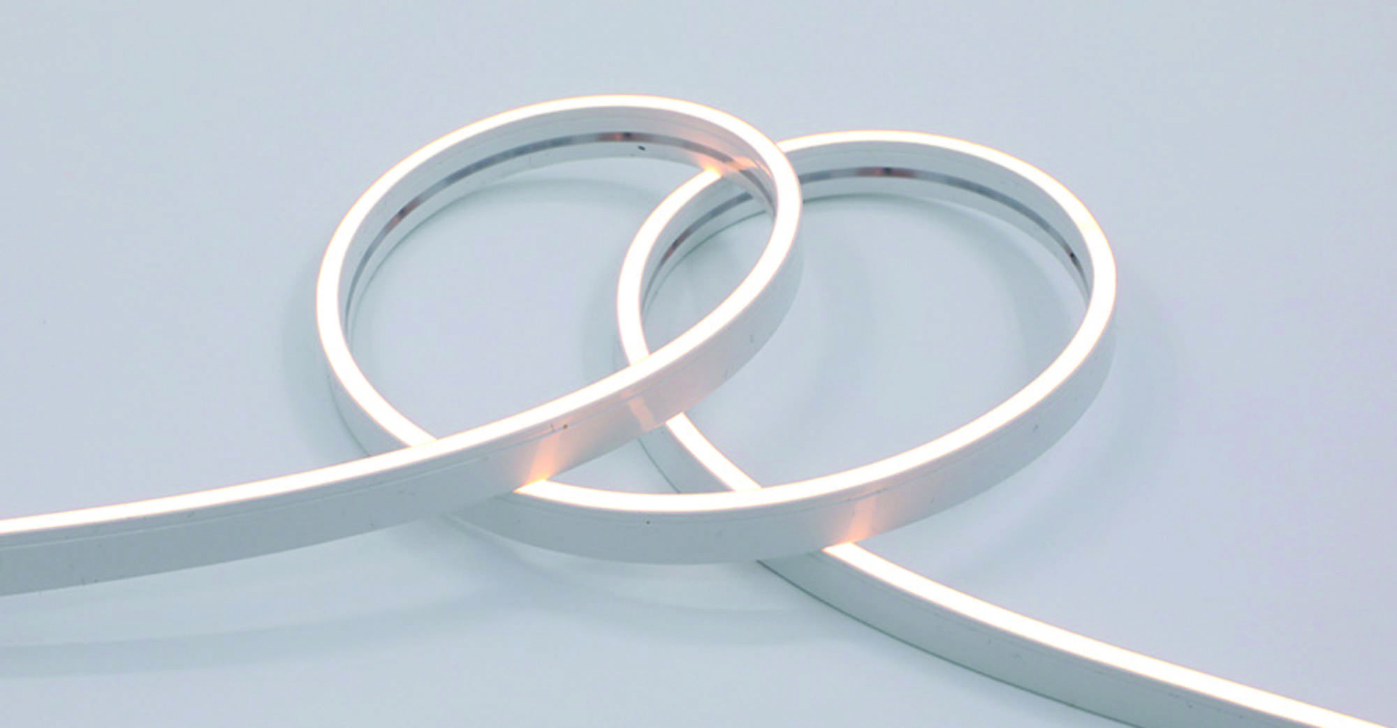 Ein aufgewickelter weißer LED-Streifenlichter auf hellgrauem Hintergrund, sanft leuchtend, zeigt seine Flexibilität und Beleuchtungsfähigkeiten.