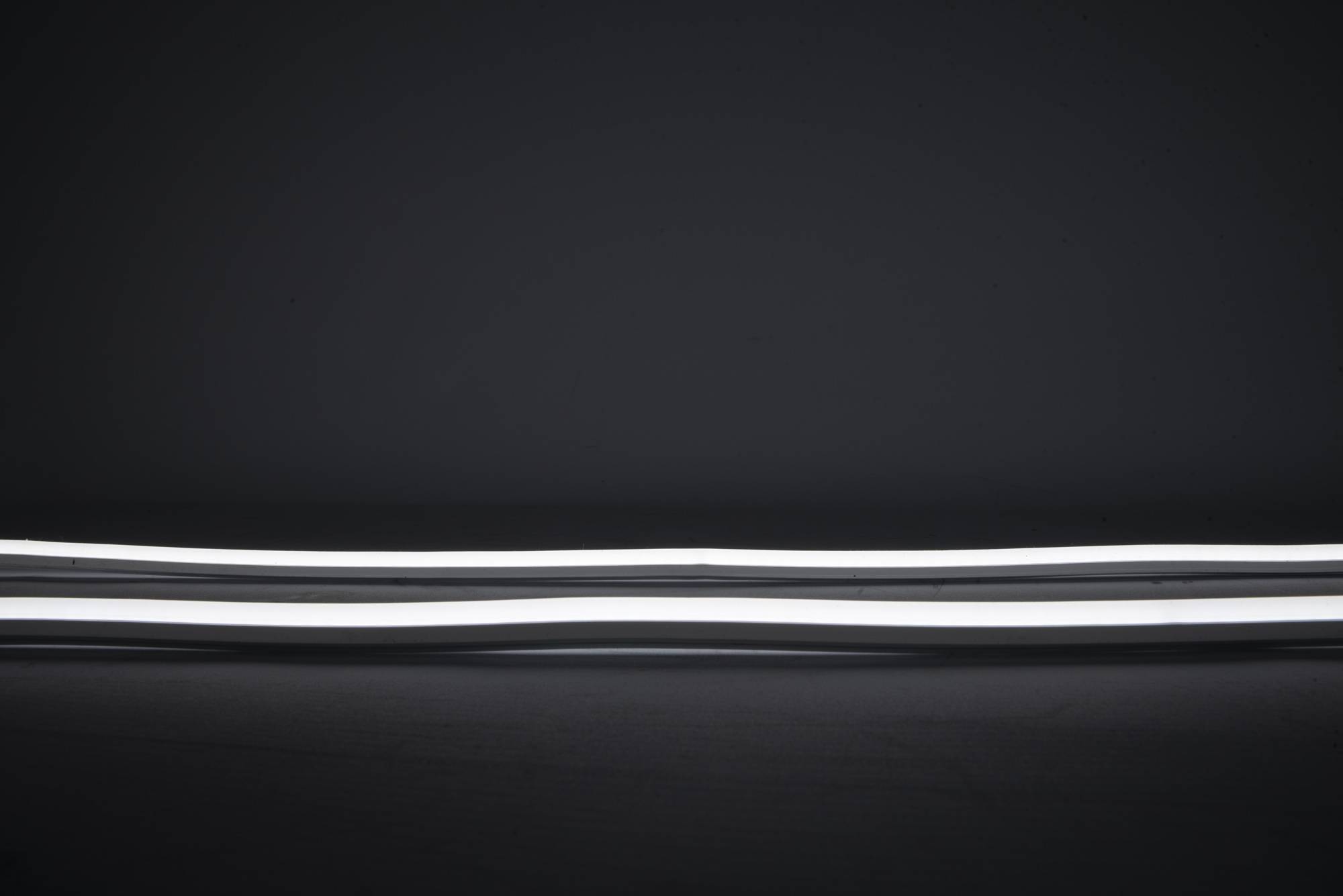 Ein gebogenes weißes Leuchtstoffrohr, horizontal gegen einen dunklen Hintergrund positioniert.