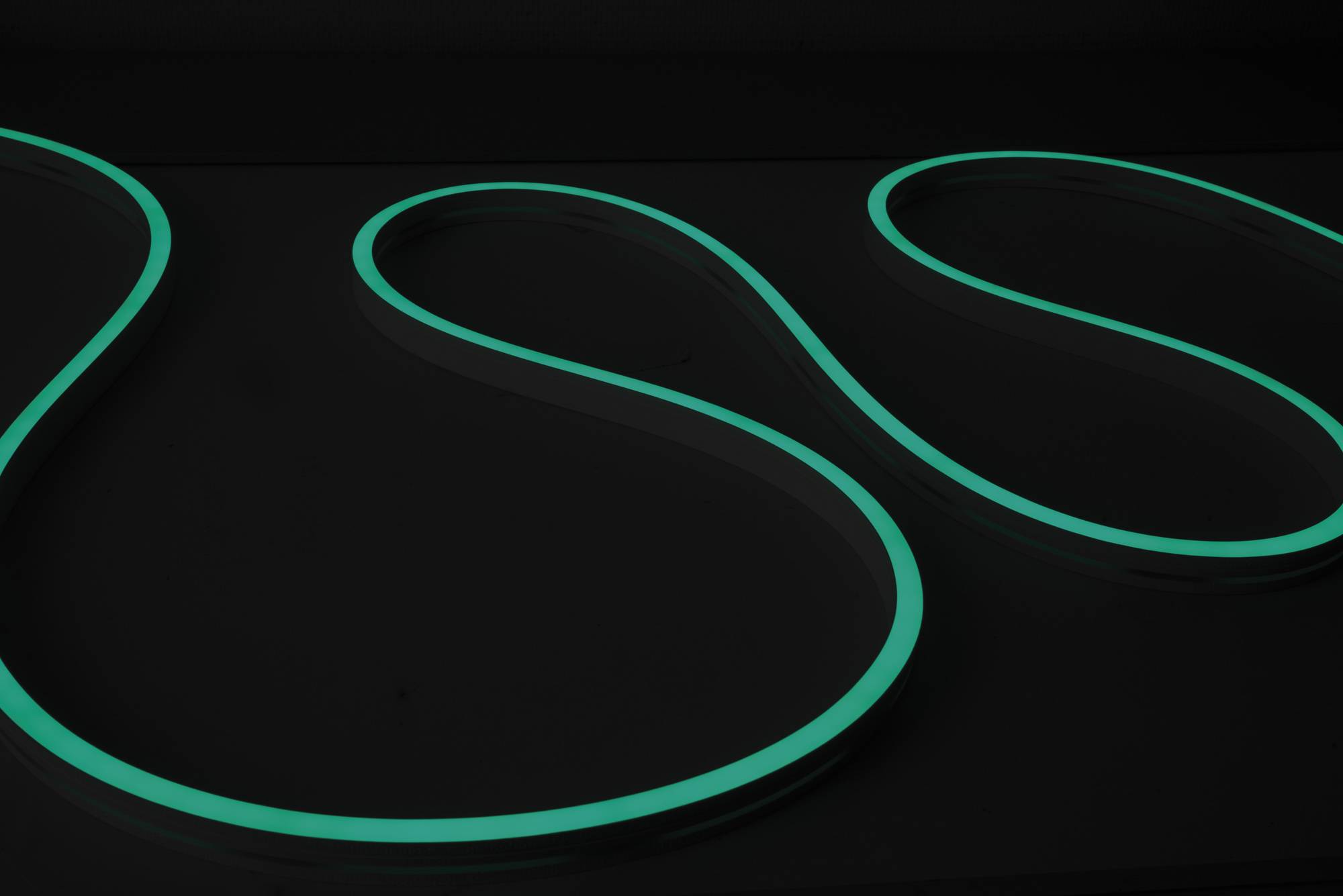 Ein leuchtendes grünes Neonlicht bildet eine glatte, sich windende S-Form gegen einen dunklen Hintergrund.