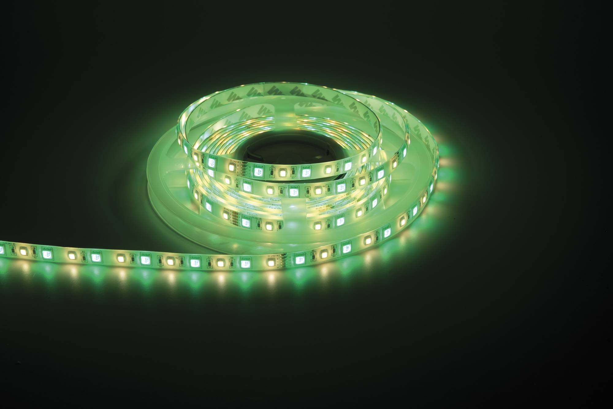 Ein leuchtender LED-Streifenleuchte auf einer dunklen Oberfläche, die grünes und weißes Licht ausstrahlt. Sauber aufgewickelt hebt sie die lebendige LED-Technologie hervor.