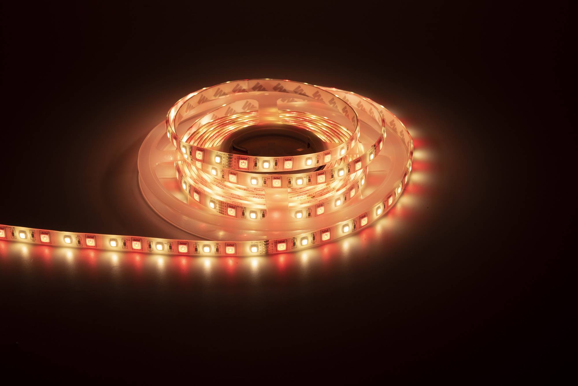 Ein aufgerolltes LED-Band, das einen warmen, rötlich-orangefarbenen Glanz gegen einen dunklen Hintergrund ausstrahlt und sein helles und flexibles Design zur Schau stellt.