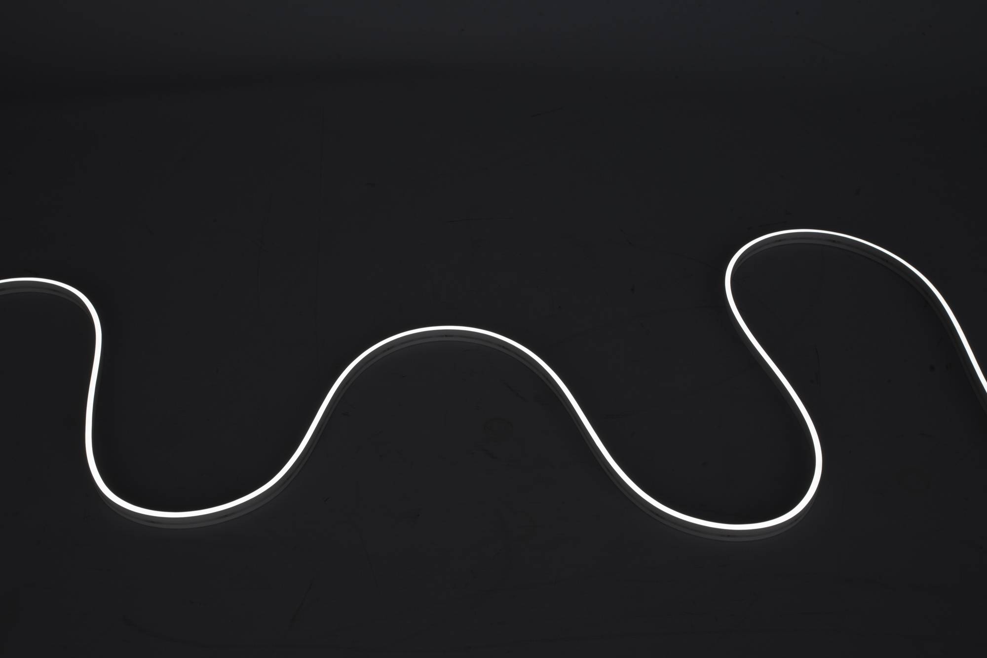 Ein leuchtendes weißes Neonlicht bildet eine wellenförmige Linie gegen einen dunklen Hintergrund und erzeugt ein abstraktes, minimalistisches Design.