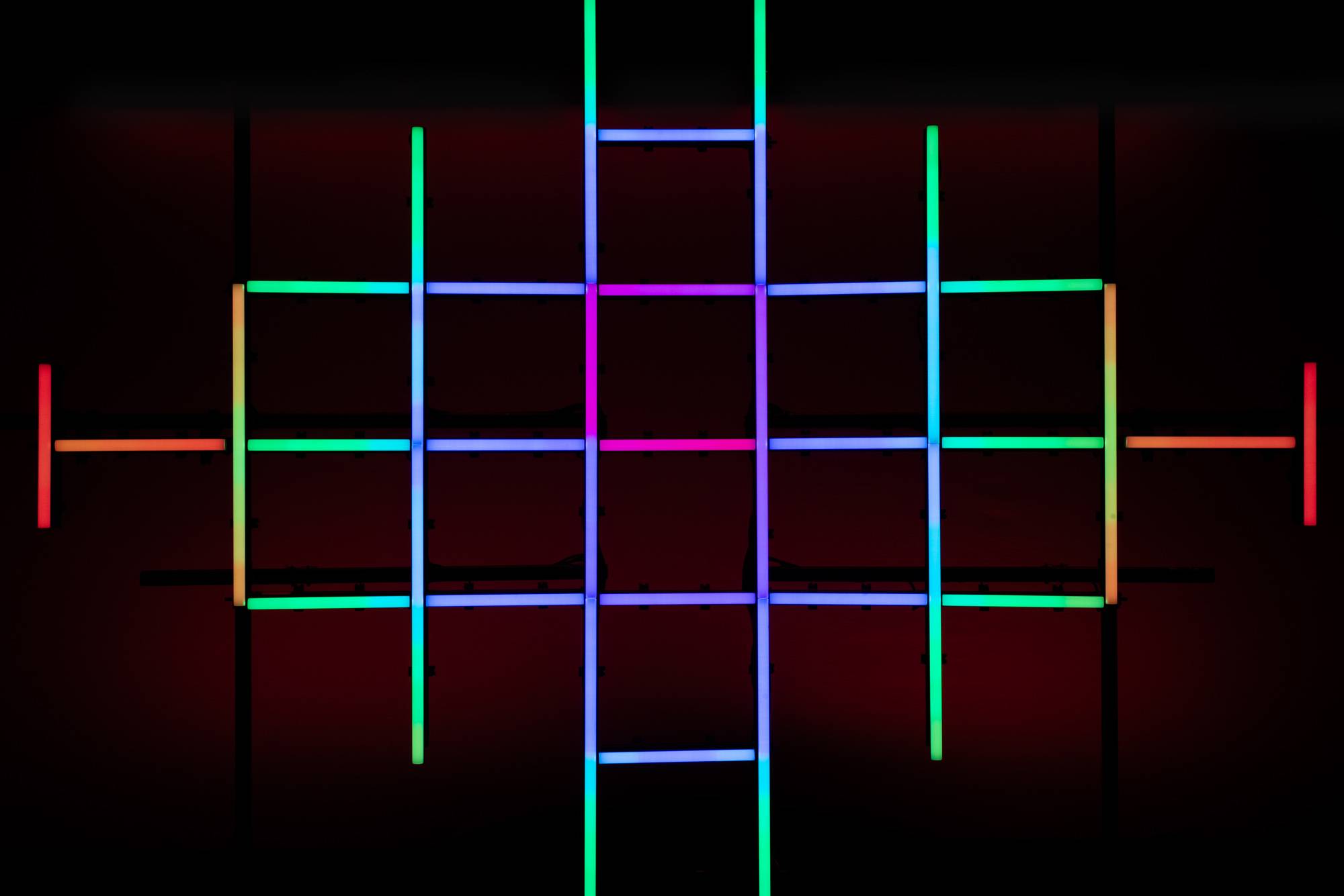 Neonlicht-Installation mit sich kreuzenden Linien in Grün, Blau, Rosa und Orange vor dunklem Hintergrund, die ein Rastermuster bilden.