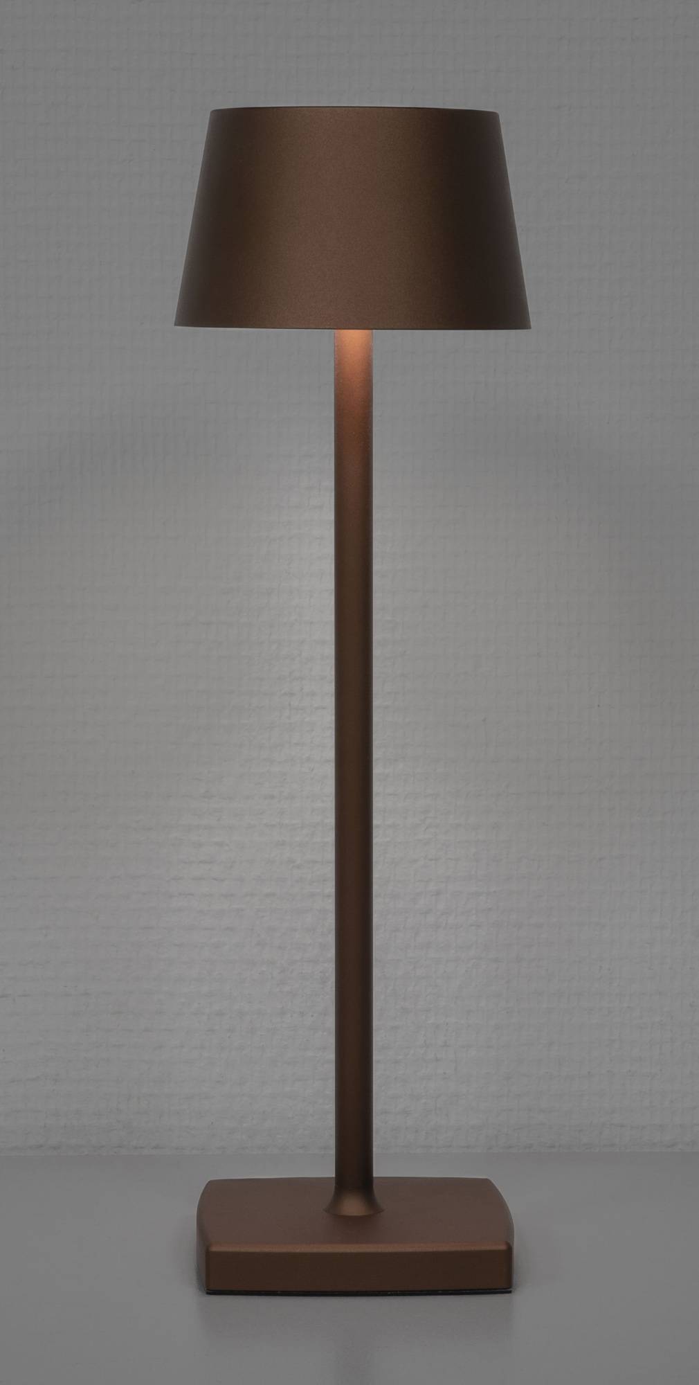 Eine hohe, schlanke Stehleuchte mit hölzernem Sockel und diffusem Licht wirft einen warmen Glanz gegen eine strukturierte, hellgraue Wand.