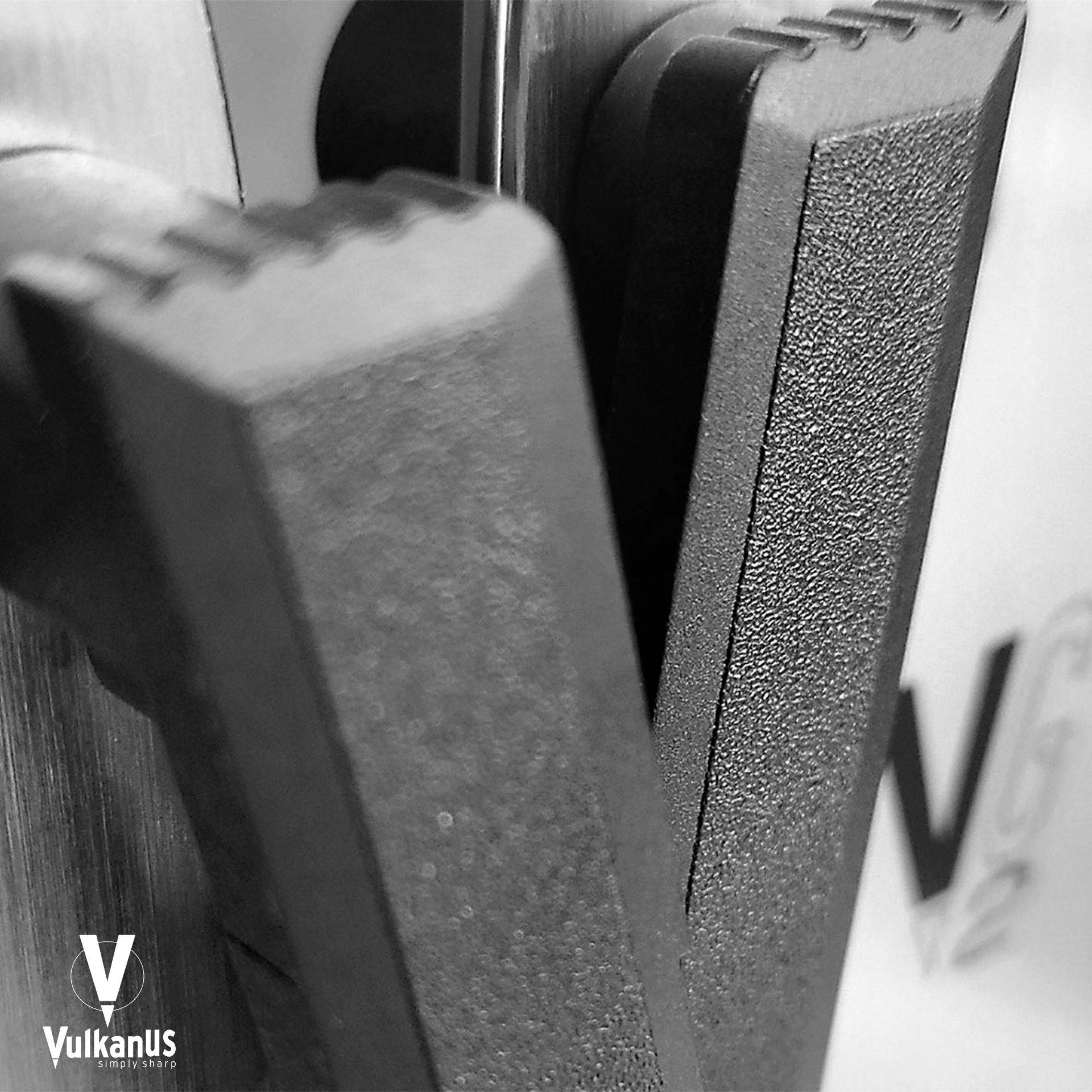 Nahaufnahme von zwei schwarzen, strukturierten Türgriffen auf einer Metalloberfläche, mit dem teilweise sichtbaren Logo „VulkanUS