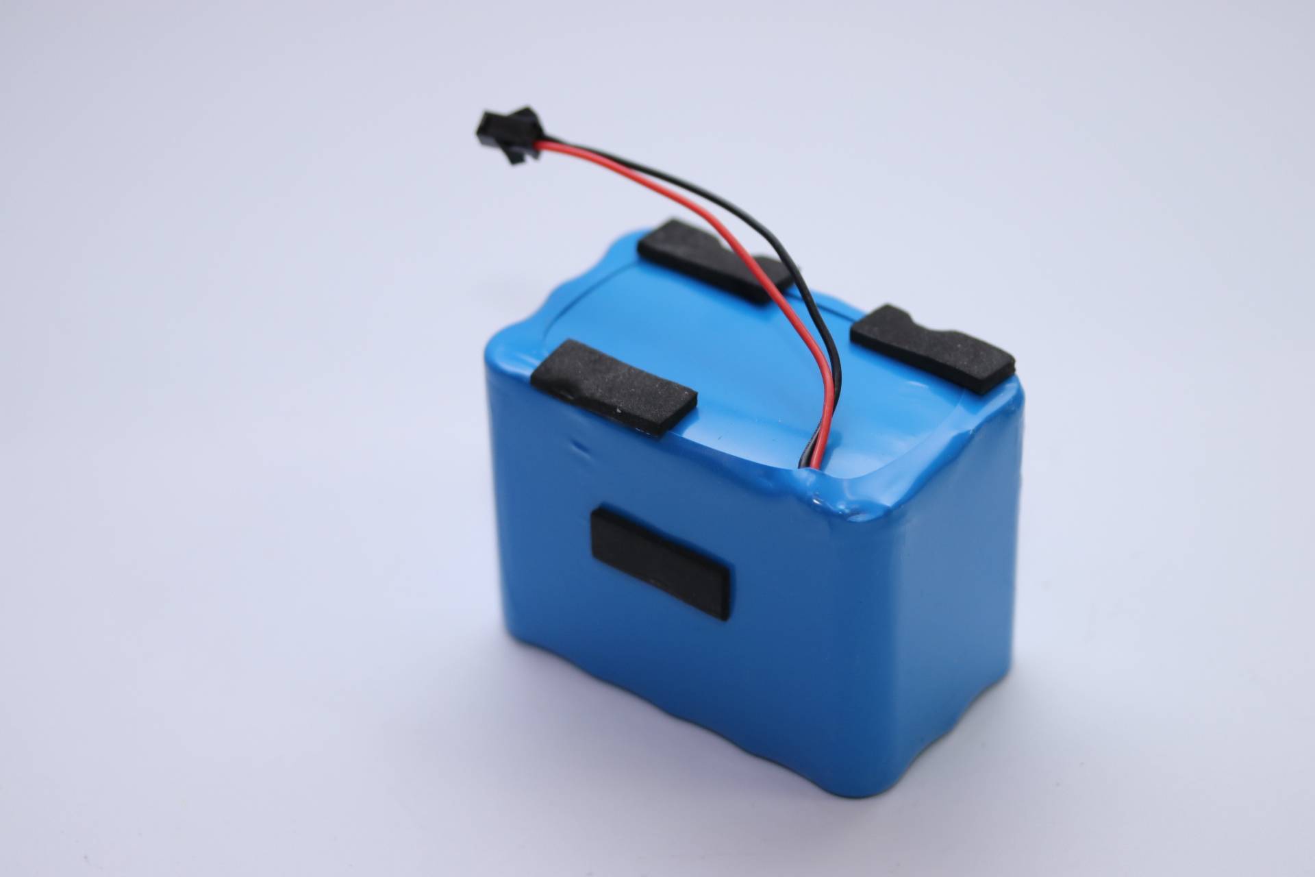Ein blaues rechteckiges Batteriepaket mit schwarzen Schaumstoffpolstern und roten und schwarzen Drähten, die oben herausragen.