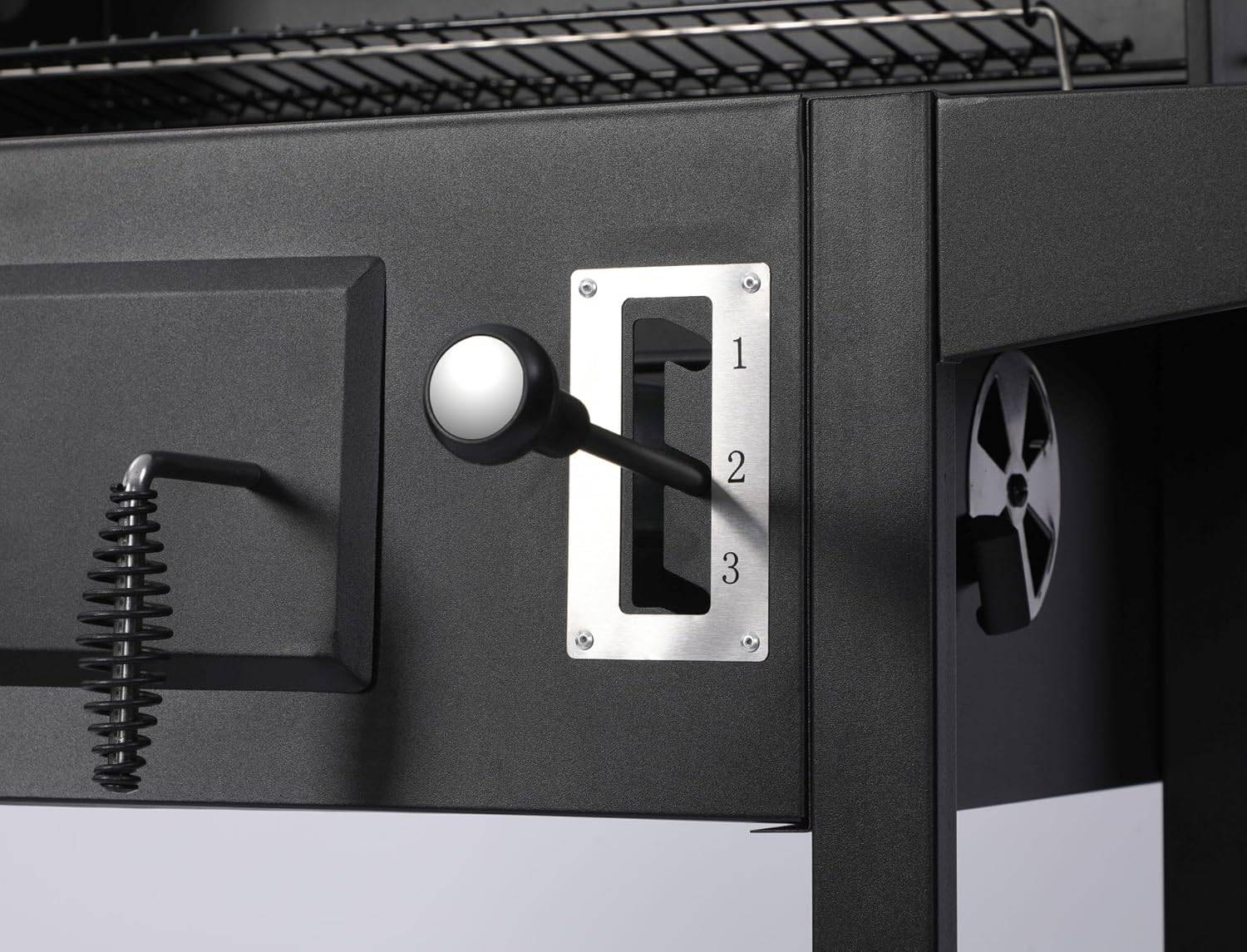 Eine Nahaufnahme eines schwarzen Metallhebels mit rundem Griff auf einem Holzkohlengrill, gekennzeichnet mit drei Einstellungen mit den Beschriftungen '1', '2' und '3'.