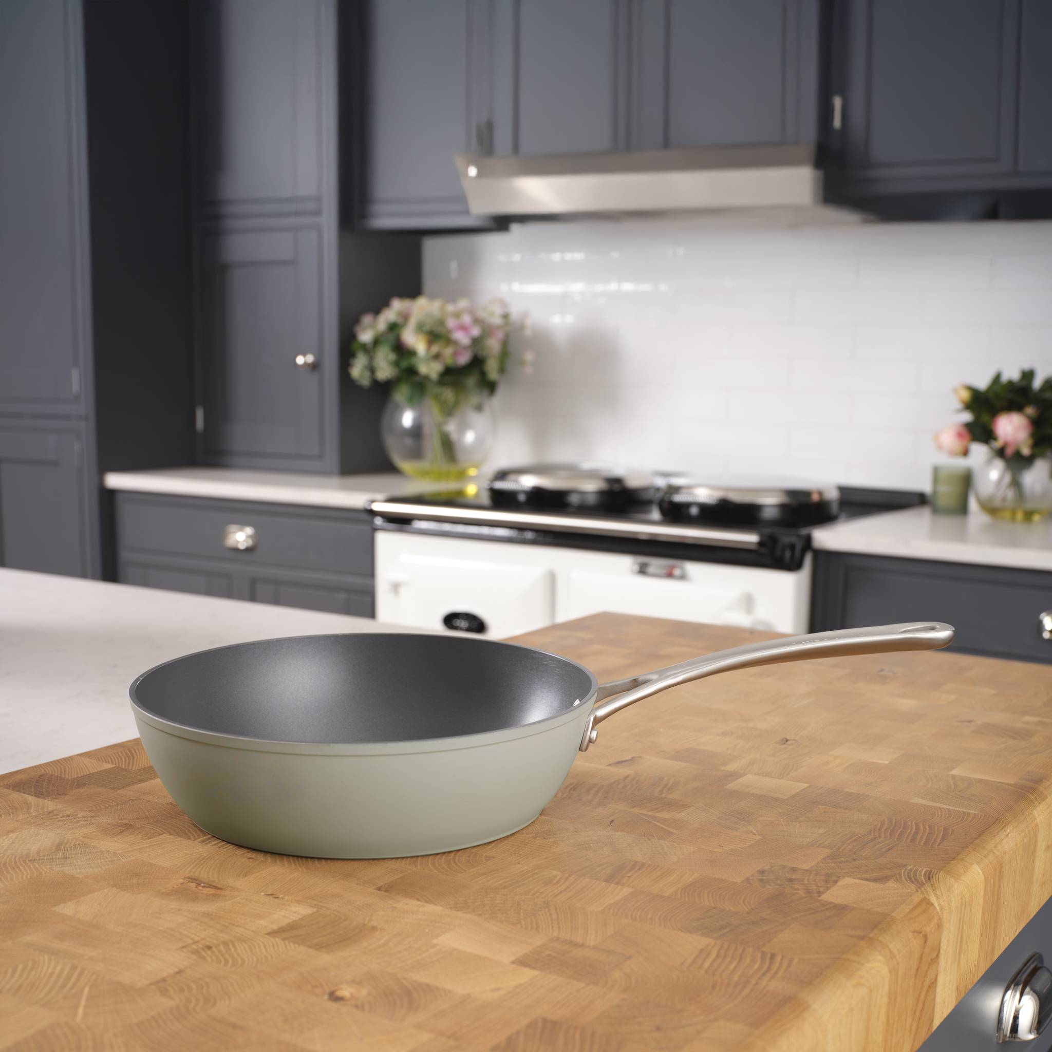 Eine antihaftbeschichtete Bratpfanne sitzt auf einer Holzarbeitsplatte in einer Küche mit weißen Schränken und modernen Geräten im Hintergrund.