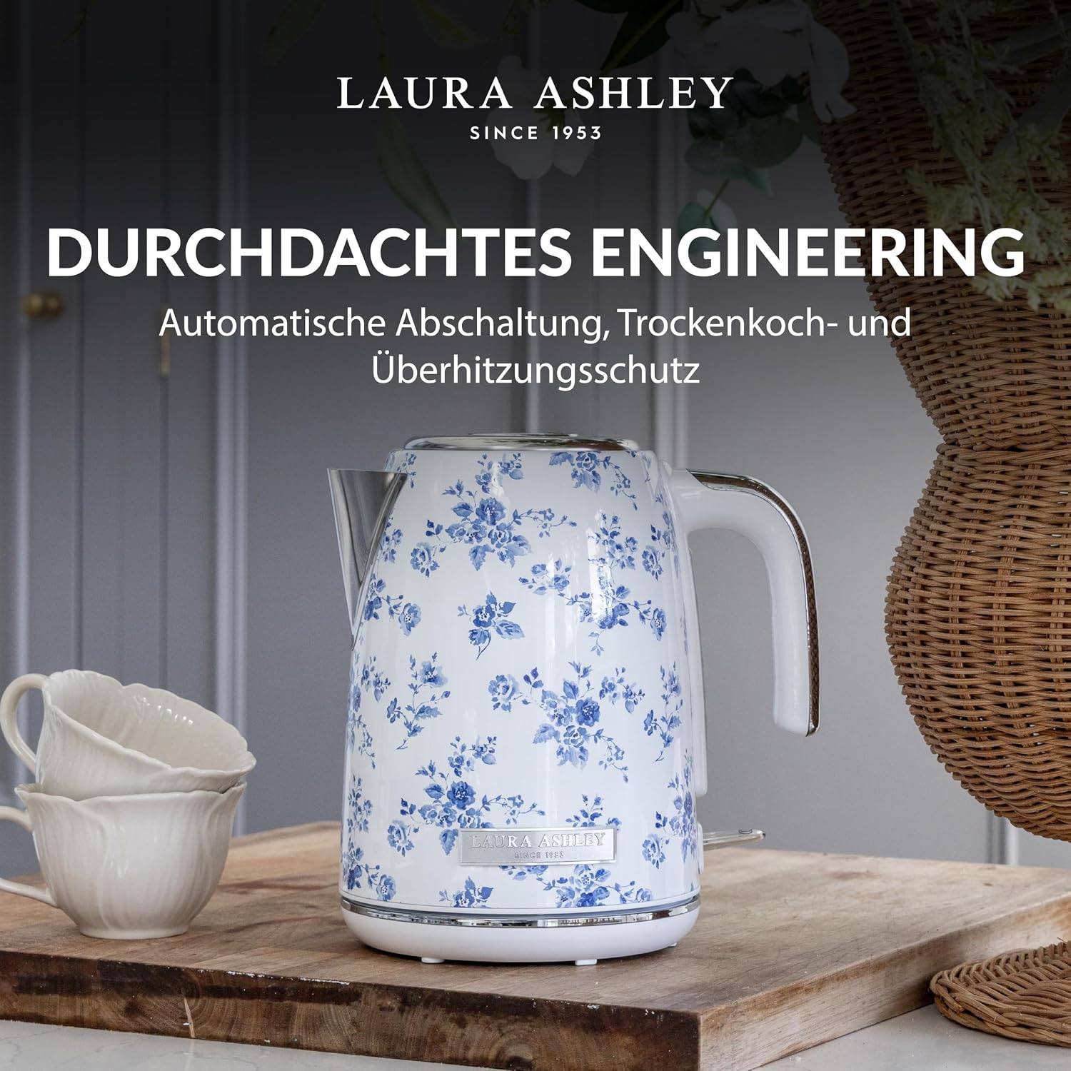 Laura Ashley Blumenmuster-Elektrokessel auf einem rustikalen Tisch mit Tassen; die Anzeigentext lautet „DURCHDACHTES ENGINEERING" und zeigt automatische Abschaltung, Trockengehschutz und Überhitzungsschutz.