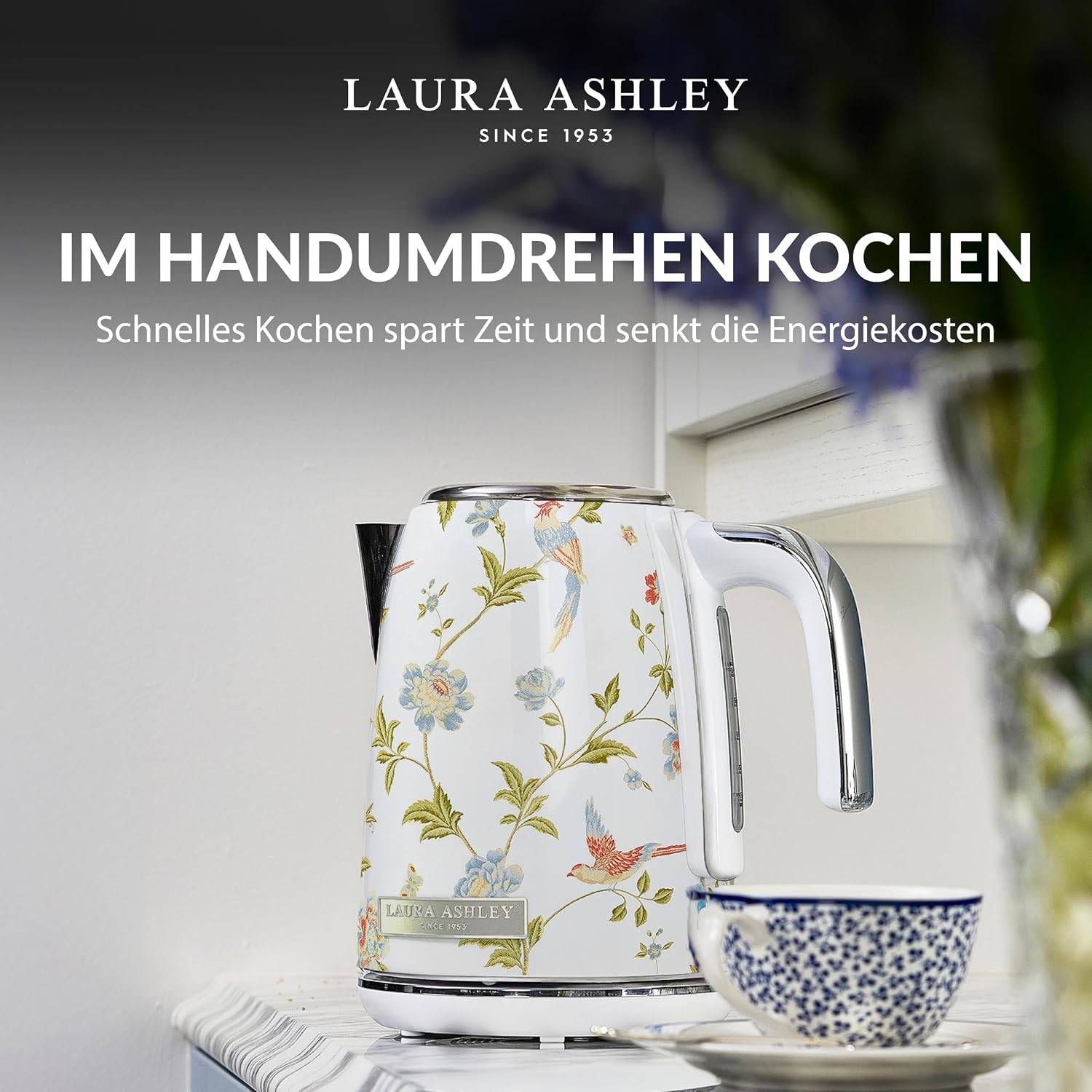 Laura Ashley Blumeneelektrokessel neben einer gemusterten Teetasse, mit deutschem Text: „Im Handumdrehen kochen" und „Schnelles Kochen spart Zeit und senkt die Energiekosten"".