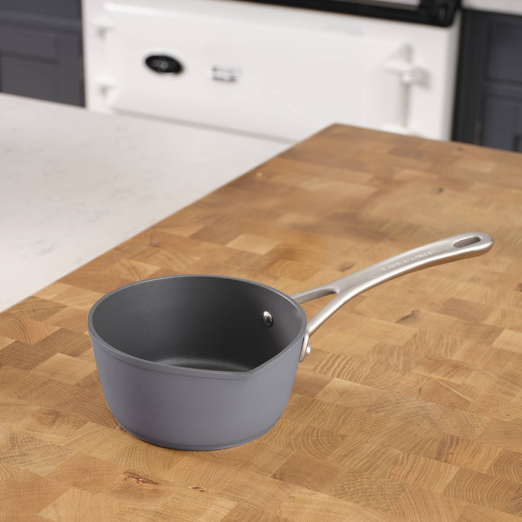 Eine graue Pfanne mit einem Metallgriff ruht auf einer Holzarbeitsplatte in einer Küche.
