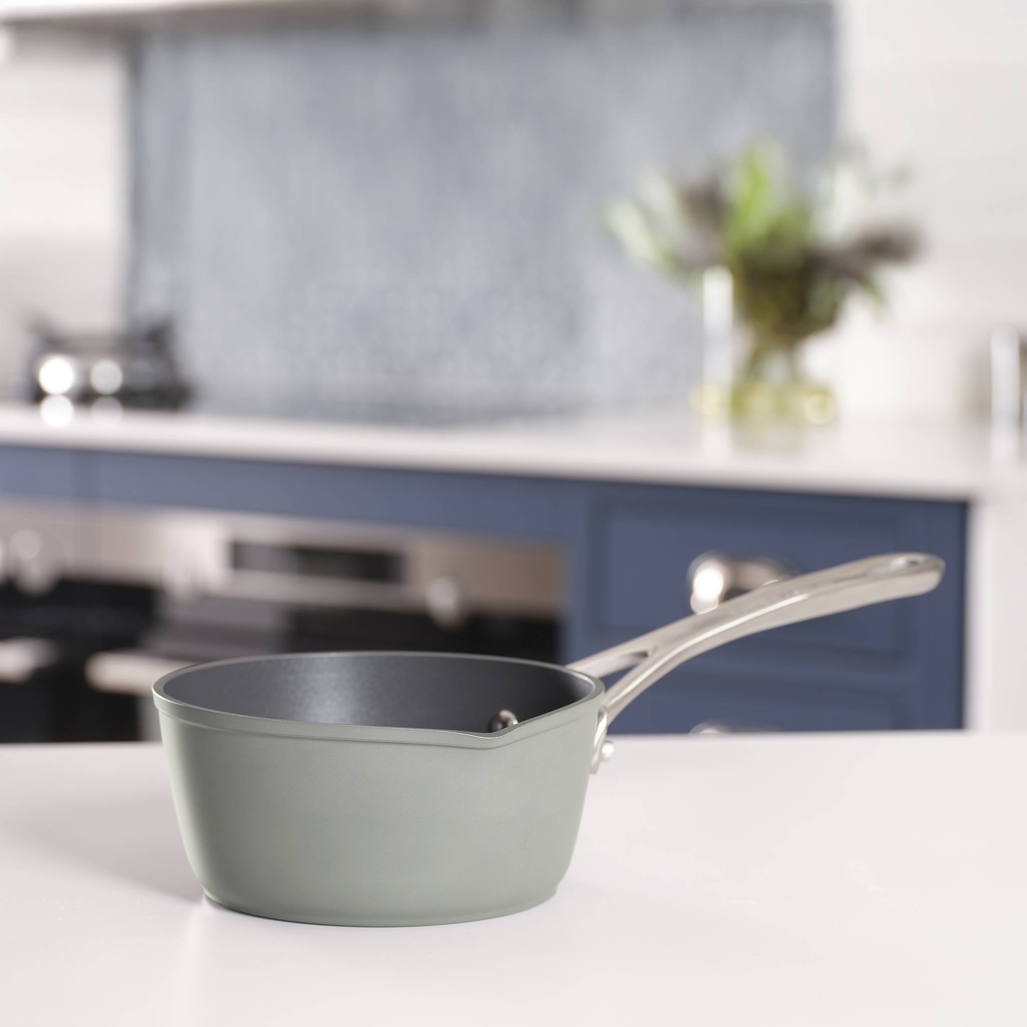 Eine graue Pfanne mit Edelstahlgriff steht auf einer weißen Arbeitsplatte in einer modernen Küche, mit unscharfem Schrank und Dekor im Hintergrund.