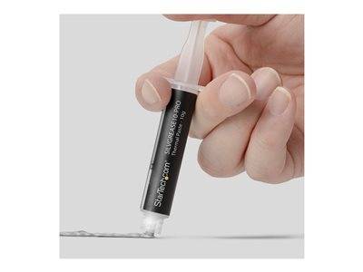 Eine Hand, die eine Spritze hält und eine silberfarbene Paste auf eine Oberfläche aufträgt. Die Spritze ist mit 