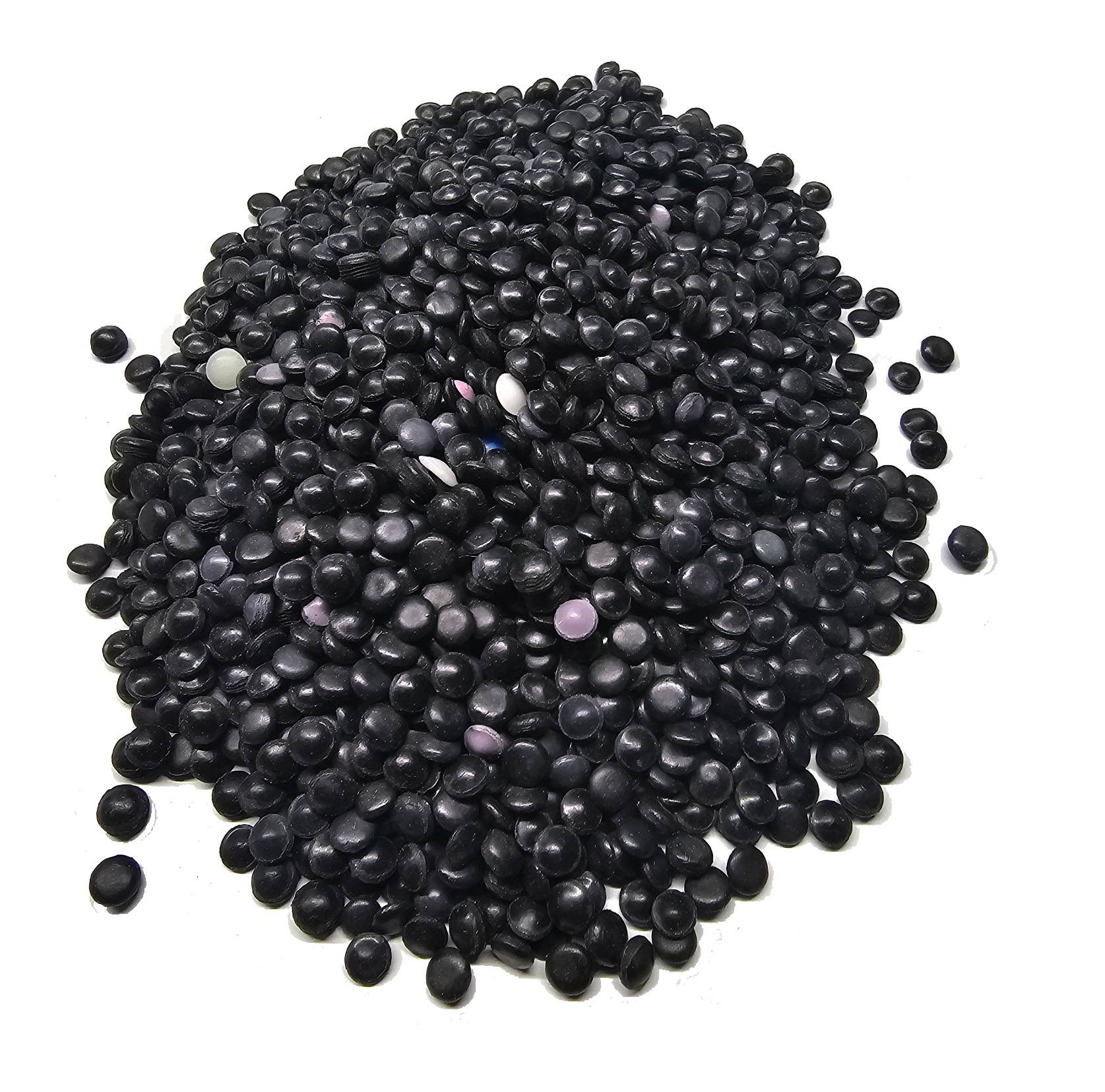 Ein Haufen kleiner, runder, schwarzer Kunstharzpellets, verstreut, mit einigen farbigen Pellets vermischt.