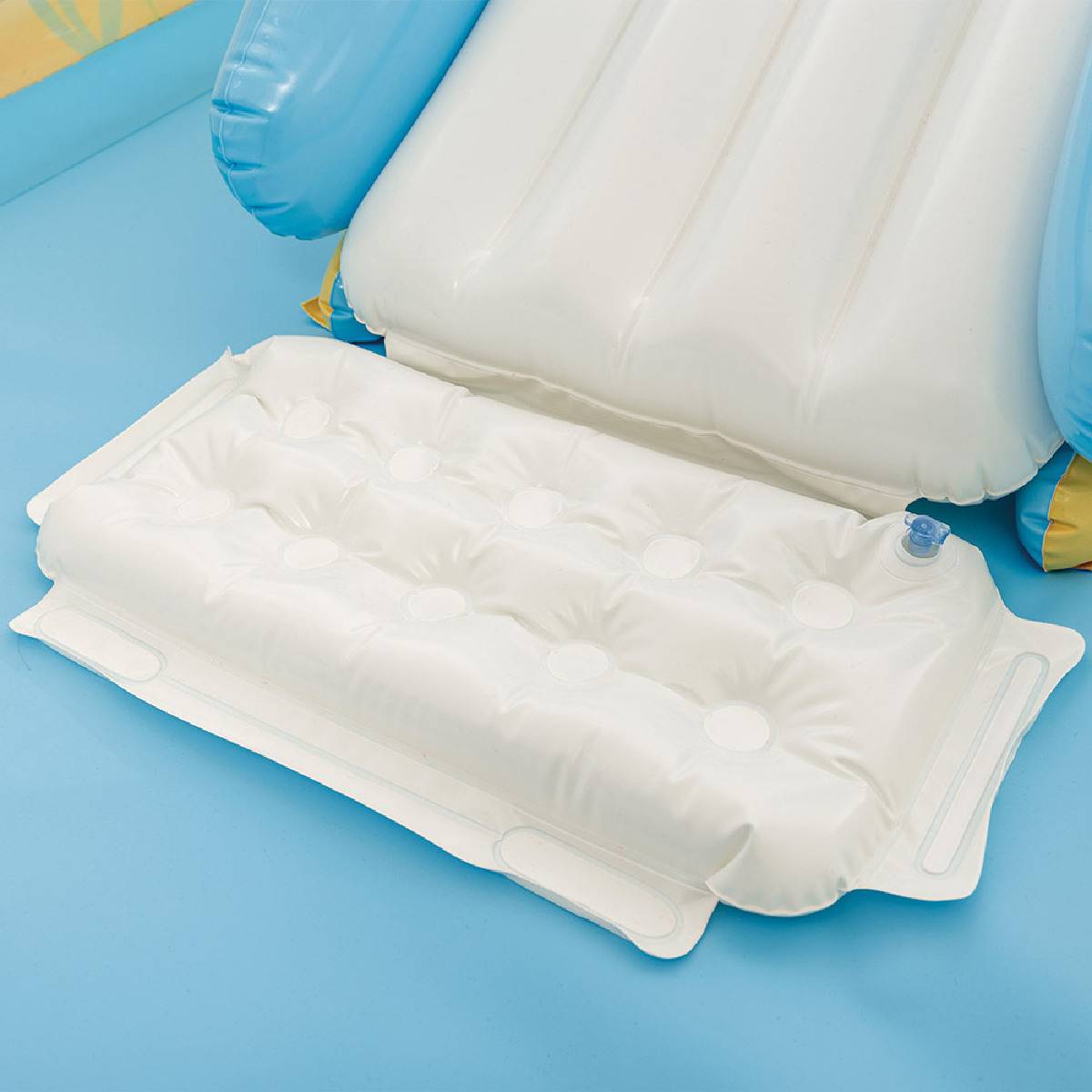 Ein aufgeblasener weißer Poolauflage ruht auf einer blauen Oberfläche und verfügt über eingebaute Kissen und Luftkammern zur Unterstützung und zum Komfort.