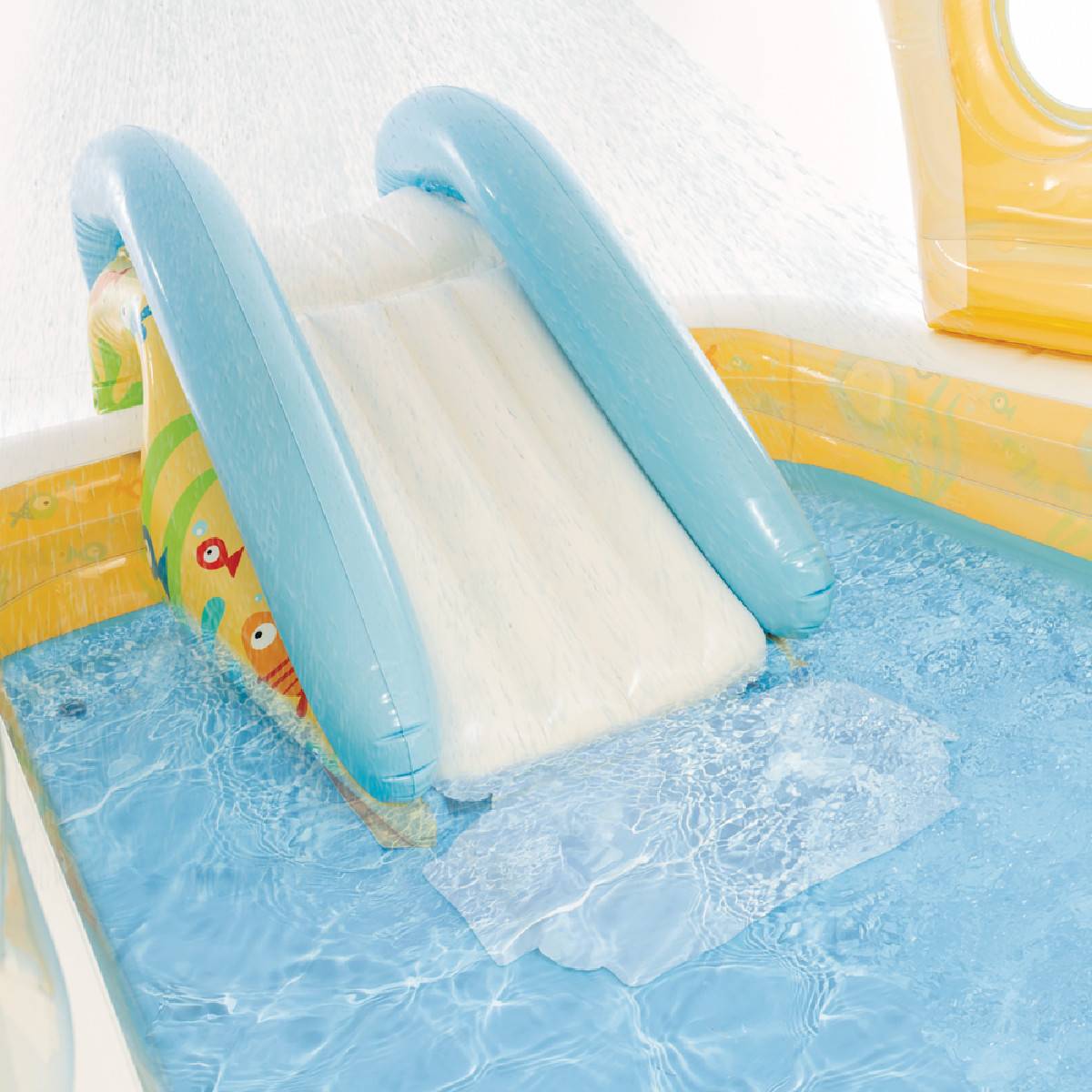 Eine leuchtend blaue und gelbe aufblasbare Wasserrutsche mit sanfter Neigung in einem kleinen Pool aufgebaut, wodurch ein Spritzwasser entsteht, während das Wasser hinunterfließt.