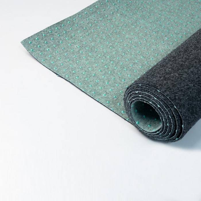 Eine Nahaufnahme eines teilweise ausgerollten grauen Teppichs mit einer gepunkteten, strukturierten Unterseite auf weißem Hintergrund.