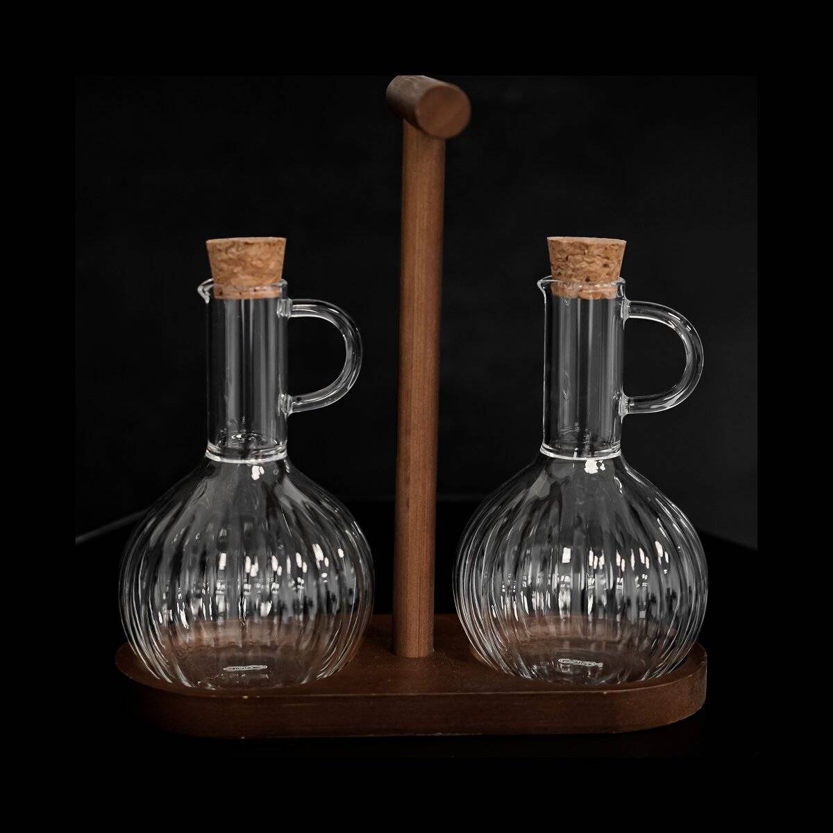 Zwei klare Glasflaschen mit Korkstopfeln stehen auf einem Holzständer und sind für Öl und Essig ausgelegt.