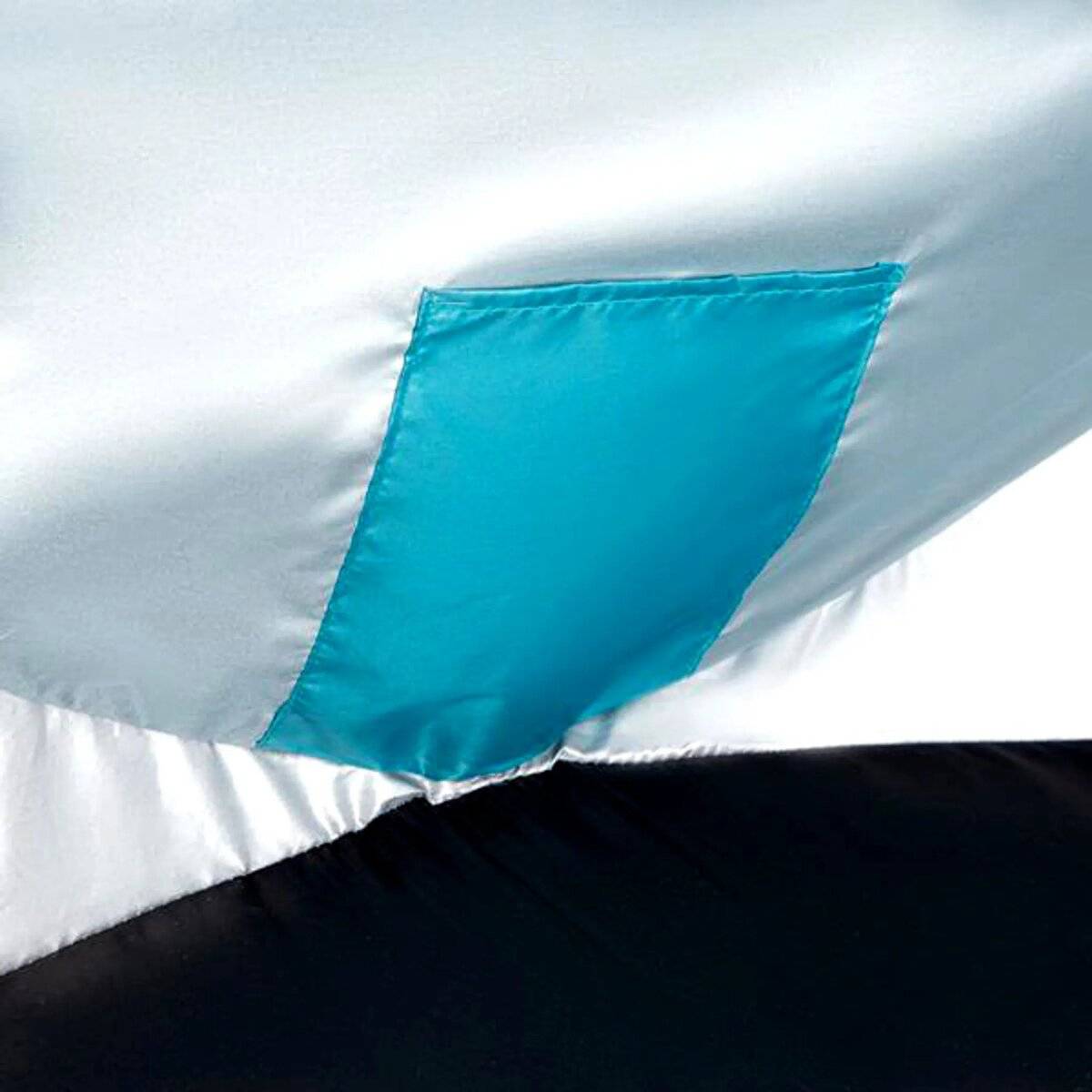 Eine Nahaufnahme eines hellblauen Satinstoffs mit glänzender Oberfläche. Ein türkisfarbener Flicken ist an der Kante aufgenäht und bildet einen Kontrast zum Hintergrund.