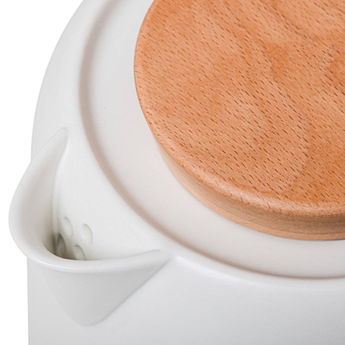 Ein weißer elektrischer Wasserkocher auf einem Holztablett mit Keksen und einer Tasse Tee auf einer Küchentheke, Blumen im Hintergrund an einem sonnigen Tag.