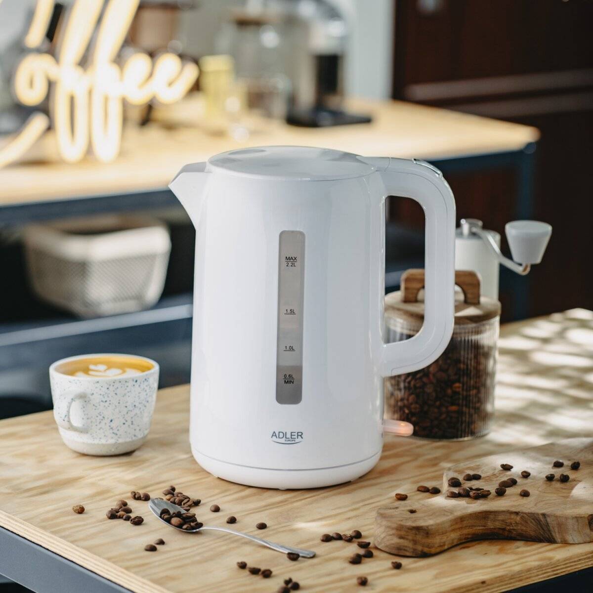 Ein weißer Wasserkocher steht auf einer Küchentheke neben einer Keramiktasse gefüllt mit Kaffee und einem durchsichtigen Behälter mit Kaffeebohnen.