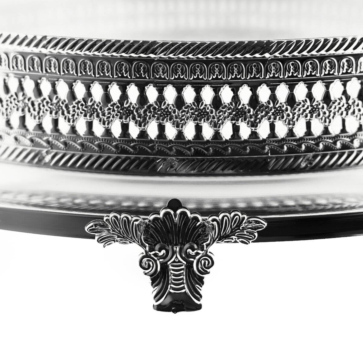 Eine verzierte, dekorative Metallkante mit aufwendigen Mustern und einem zentralen Blüten­motiv auf einer reflektierenden Oberfläche.