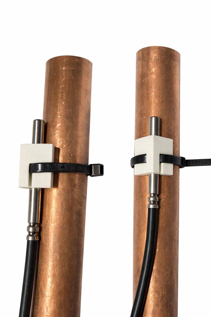 Zwei Kupferrohre mit angebrachten weißen Halterungen, schwarzen Bändern und Verbindungsstücken für sichere Befestigungen.