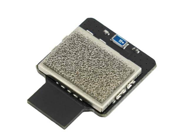 Ein kleiner Metall-Mikrochip mit einer netzförmig überdeckten Mitte, montiert auf einer schwarzen Leiterplatte, was auf technologische Komponenten hinweist.