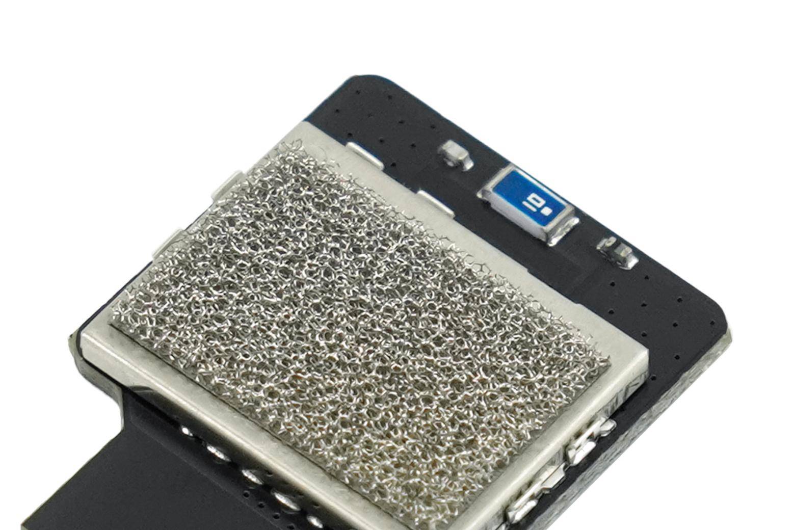 Nahaufnahme einer metallischen Maschenkomponente auf einer schwarzen Leiterplatte, wahrscheinlich ein Kühlkörper- oder Filtermodul, mit sichtbaren Schrauben und Steckverbindern.