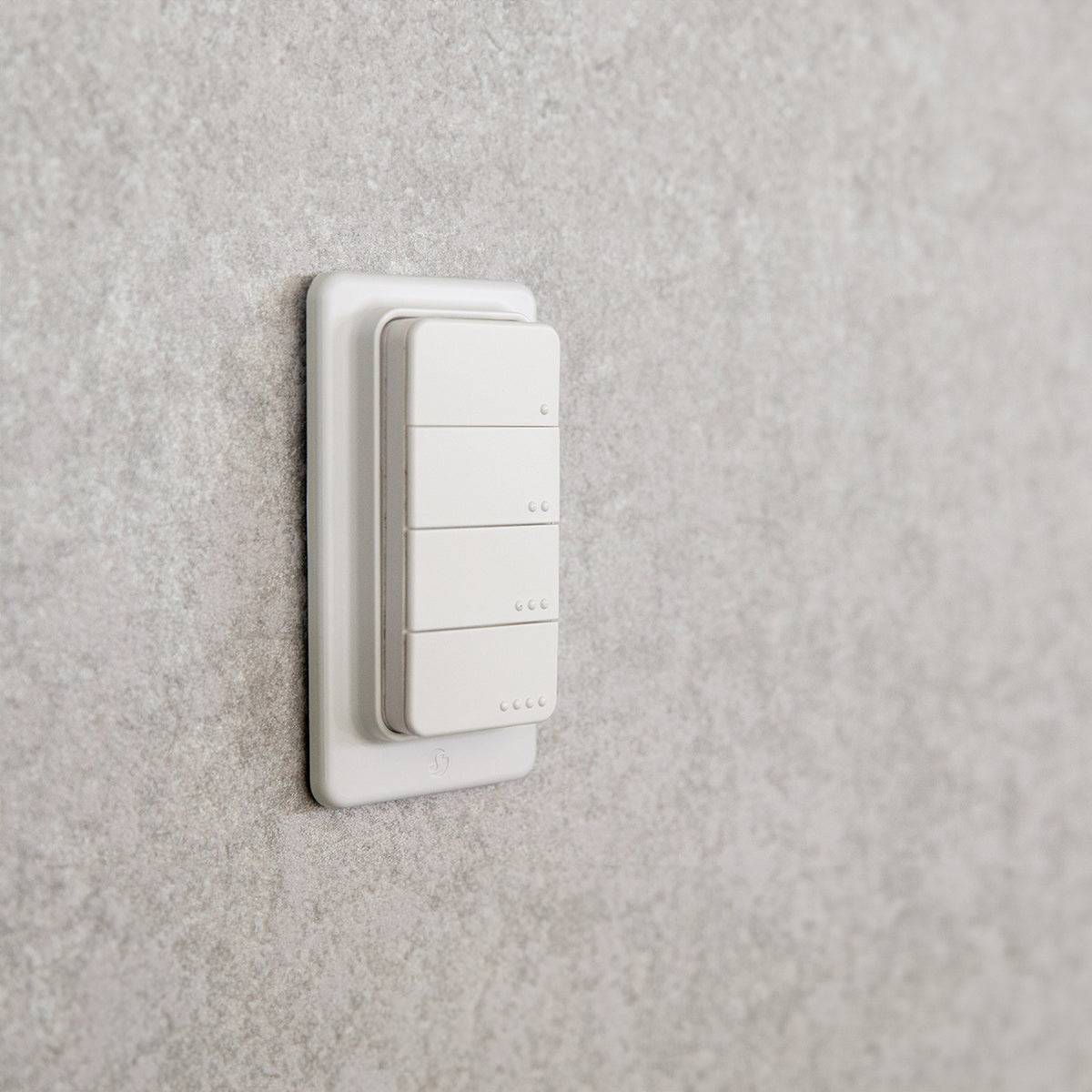 Ein weißer, rechteckiger Lichtschalter mit vier Tasten, der auf einer strukturierten grauen Wand installiert ist. Der Schalter hat ein einfaches, minimalistisches Design.