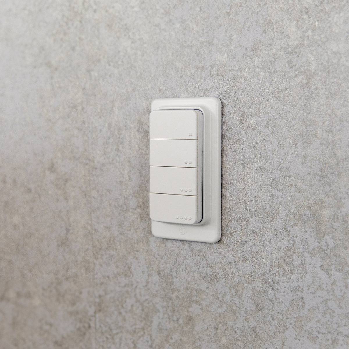 Ein weißer Lichtschalter mit mehreren Tasten, der an einer strukturierten grauen Wand angebracht ist.