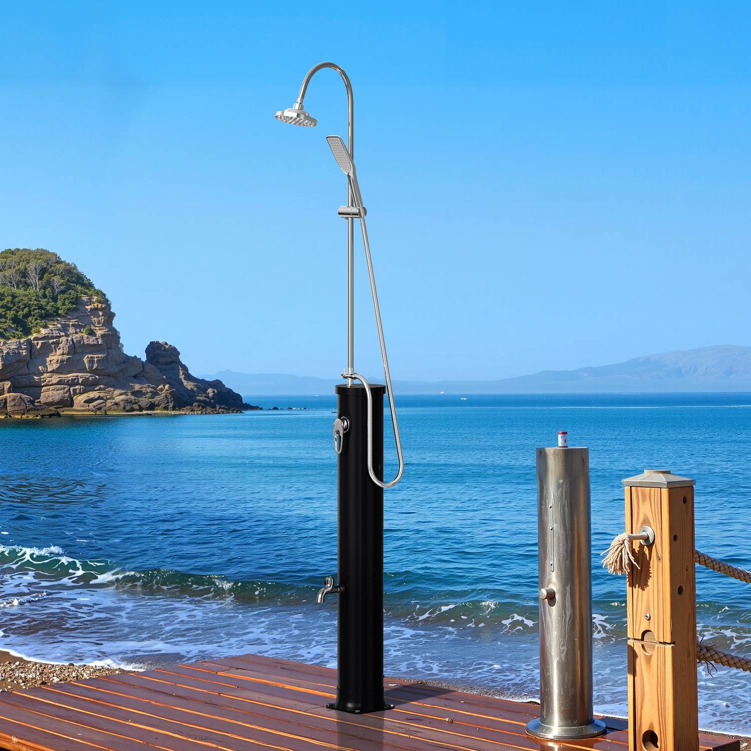 Außendusche auf einem Holzdeck an einem Strand, mit Felsklippen und ruhigen Meereswellen im Hintergrund, unter einem klaren blauen Himmel.
