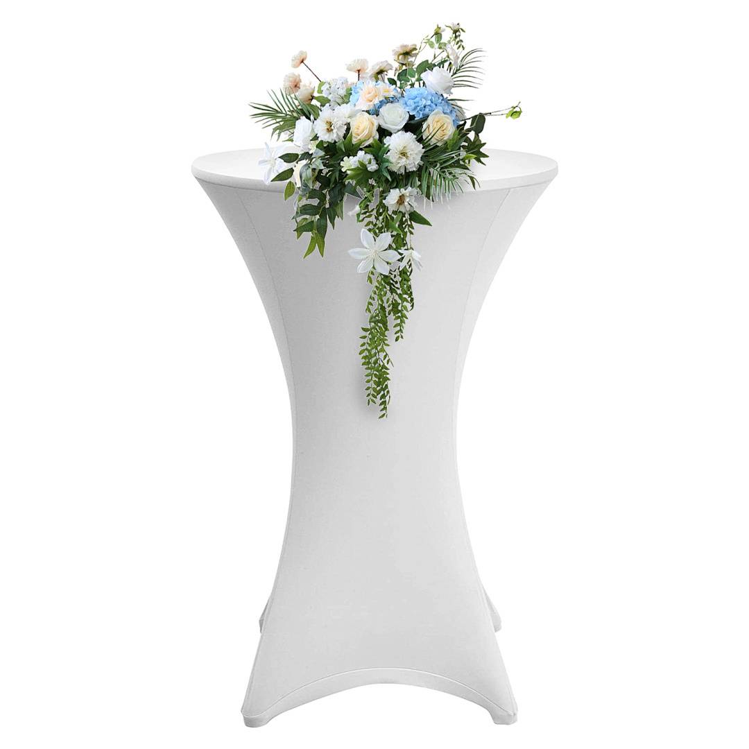 Ein großer, runder weißer Cocktailtisch, auf dem ein Blumenarrangement mit blauen und weißen Blumen sowie grünem Laub drapiert ist.