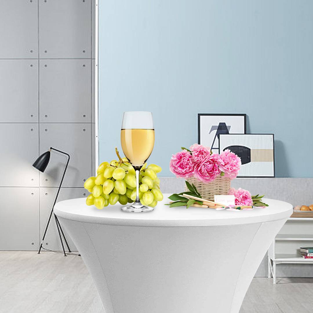 Ein weißer Sockeltisch mit einem Glas Wein, Trauben, einem Korb mit rosa Blumen und Kunstbedarf, aufgestellt in einem modernen Zimmer mit Wanddekoration.