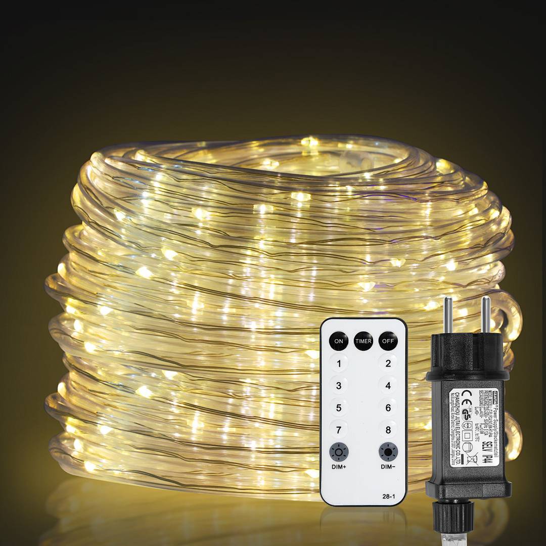 Eine Spule mit leuchtenden Lichterketten mit einer Fernbedienung und einem Steckeradapter vor dunklem Hintergrund.