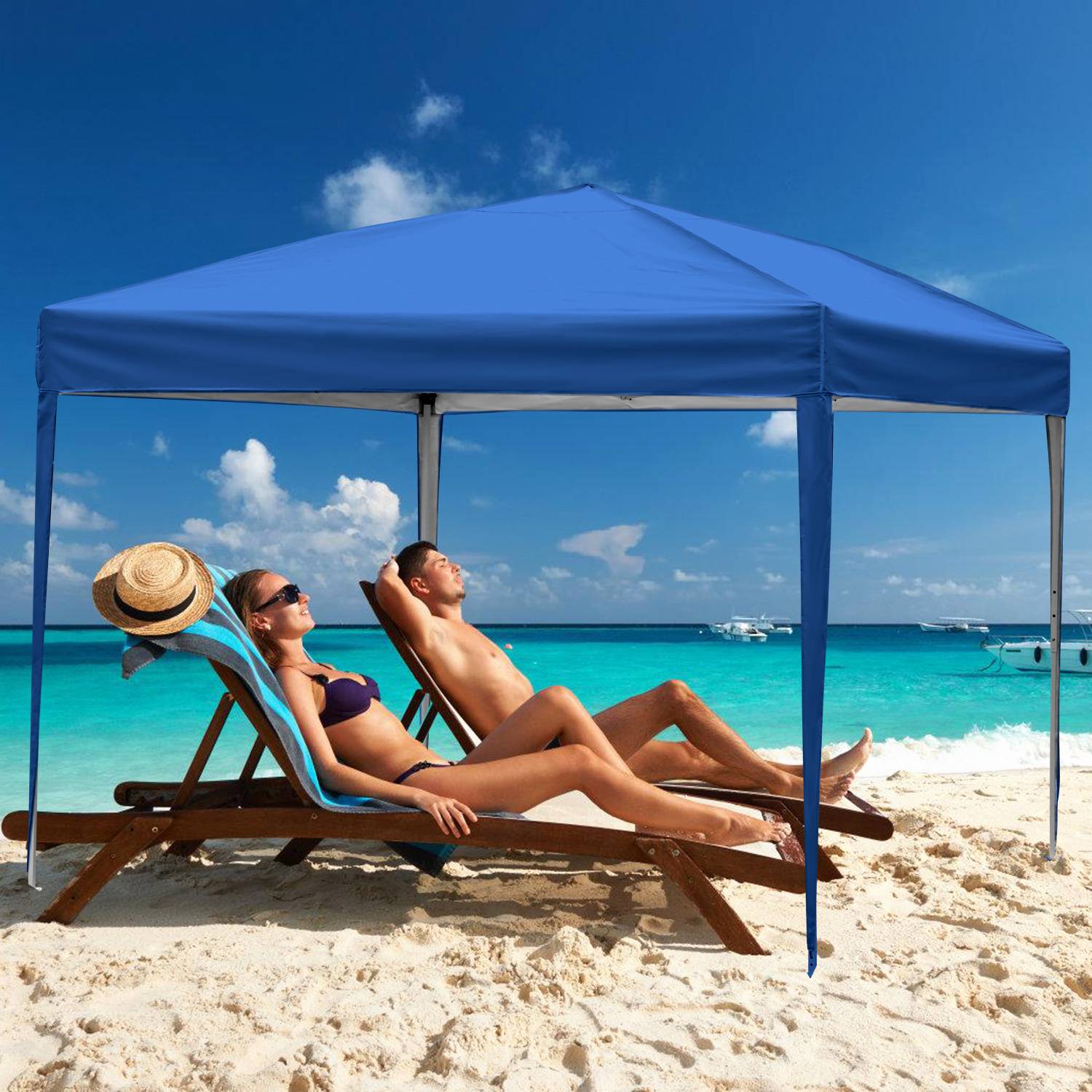 Ein Paar entspannt sich auf Liegestühlen unter einem blauen Sonnendach auf einem sandigen Strand, mit einem lebendigen türkisfarbenen Meer und teilweise bewölktem Himmel im Hintergrund.