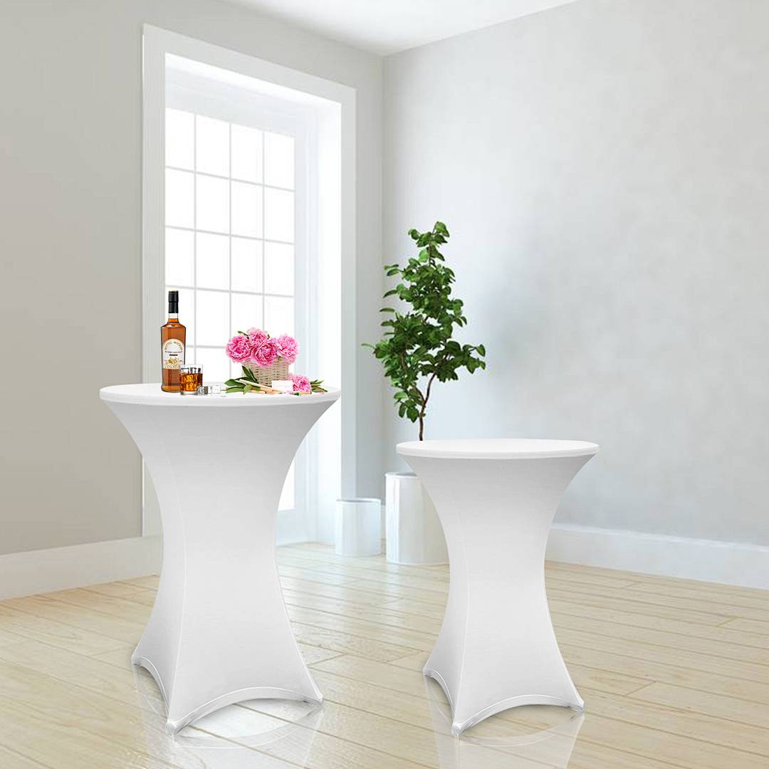 Zwei runde, weiße Tische sind mit Tischdecken bezogen. Einer hält eine Flasche und rosa Blumen, und eine Topfpflanze steht auf dem Boden in der Nähe.