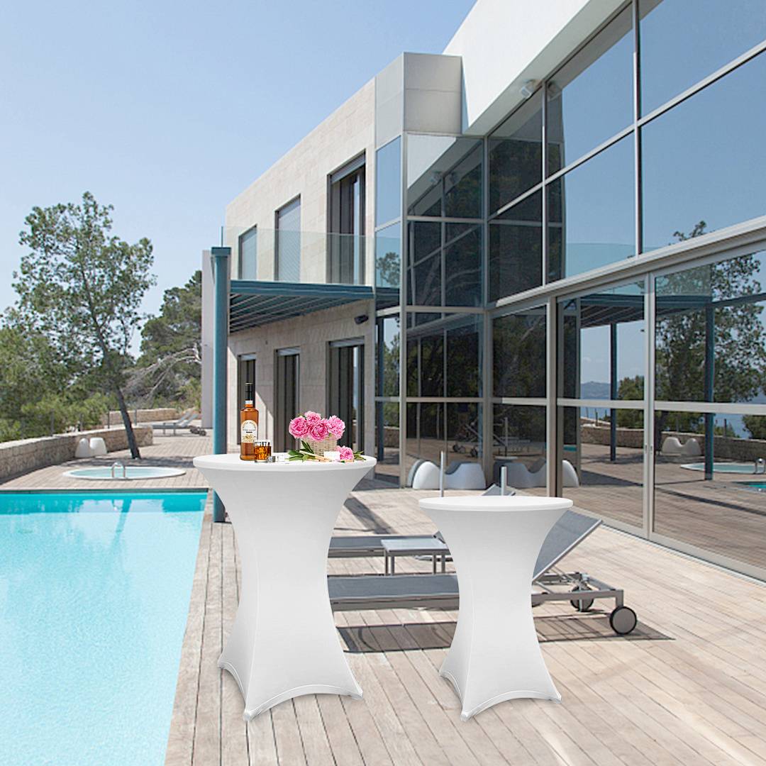 Eine moderne Terrasse mit zwei Cocktailtischen neben einem Schwimmbad, angrenzend an ein zeitgenössisches Haus aus Glas und Beton.