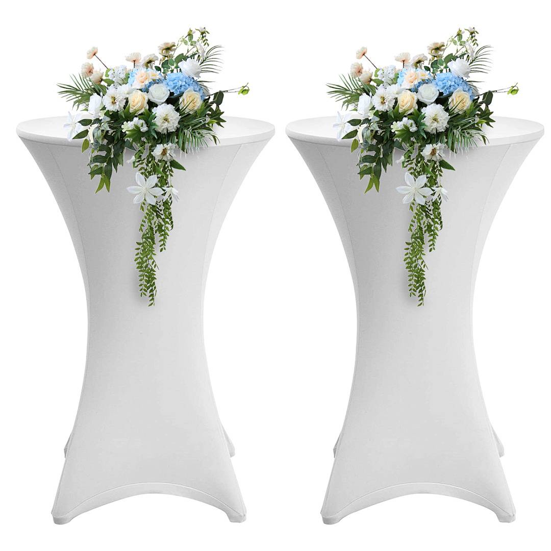 Zwei hohe weiße Tische sind mit Blumenarrangements geschmückt, die weiße, blaue und rosa Blüten sowie herabfallendes Grün aufweisen.