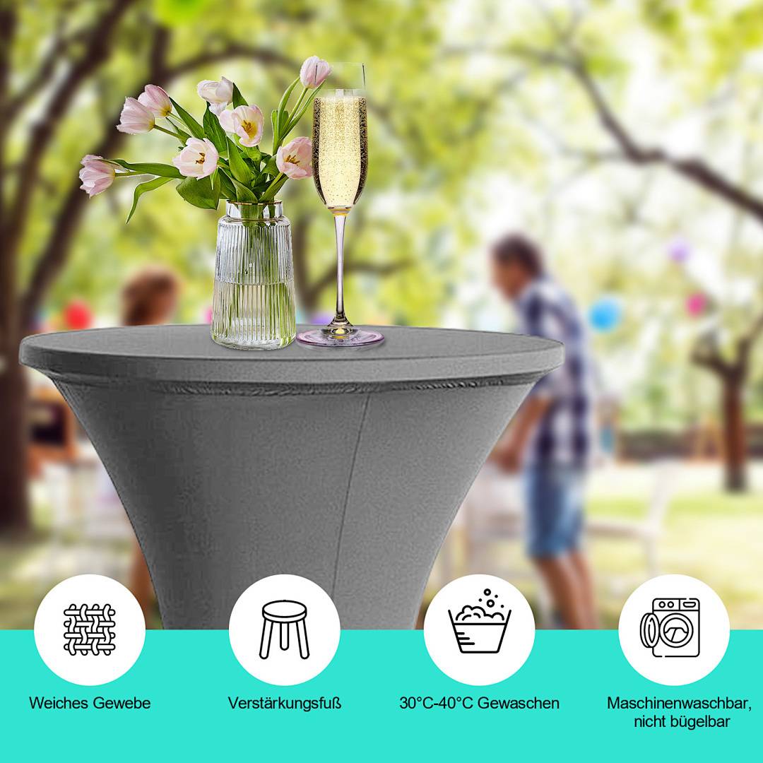 Ein Cocktailtisch mit grauem Bezug hält eine Blumenvase und ein Glas Champagner. Der unscharfe Hintergrund zeigt Menschen bei einer Außenveranstaltung.