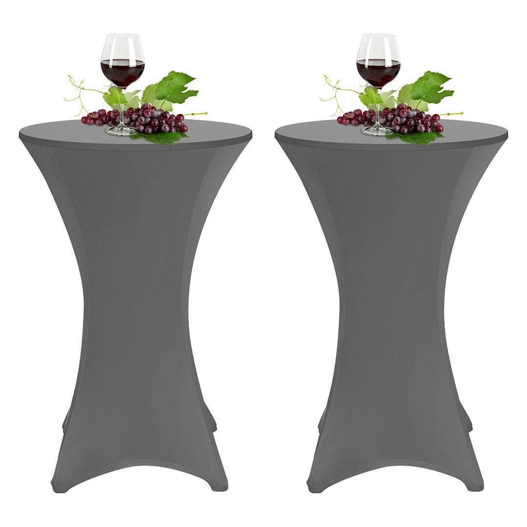 Zwei hohe runde Tische mit grauen Abdeckungen, jeder mit einem Weinglas gefüllt mit Rotwein, Traubenbündeln und grünen Blättern obenauf.