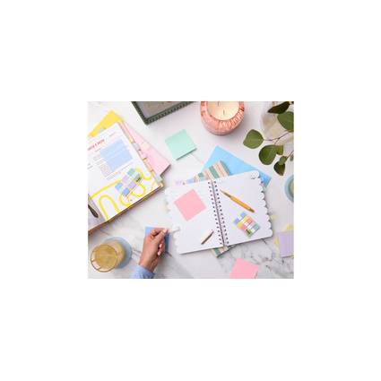 Ein offener Planer mit Haftnotizen und Stiften auf einem Schreibtisch, umgeben von einer Kerze, einer Pflanze und farbenfrohen Ordnern, was auf Organisation hindeutet.