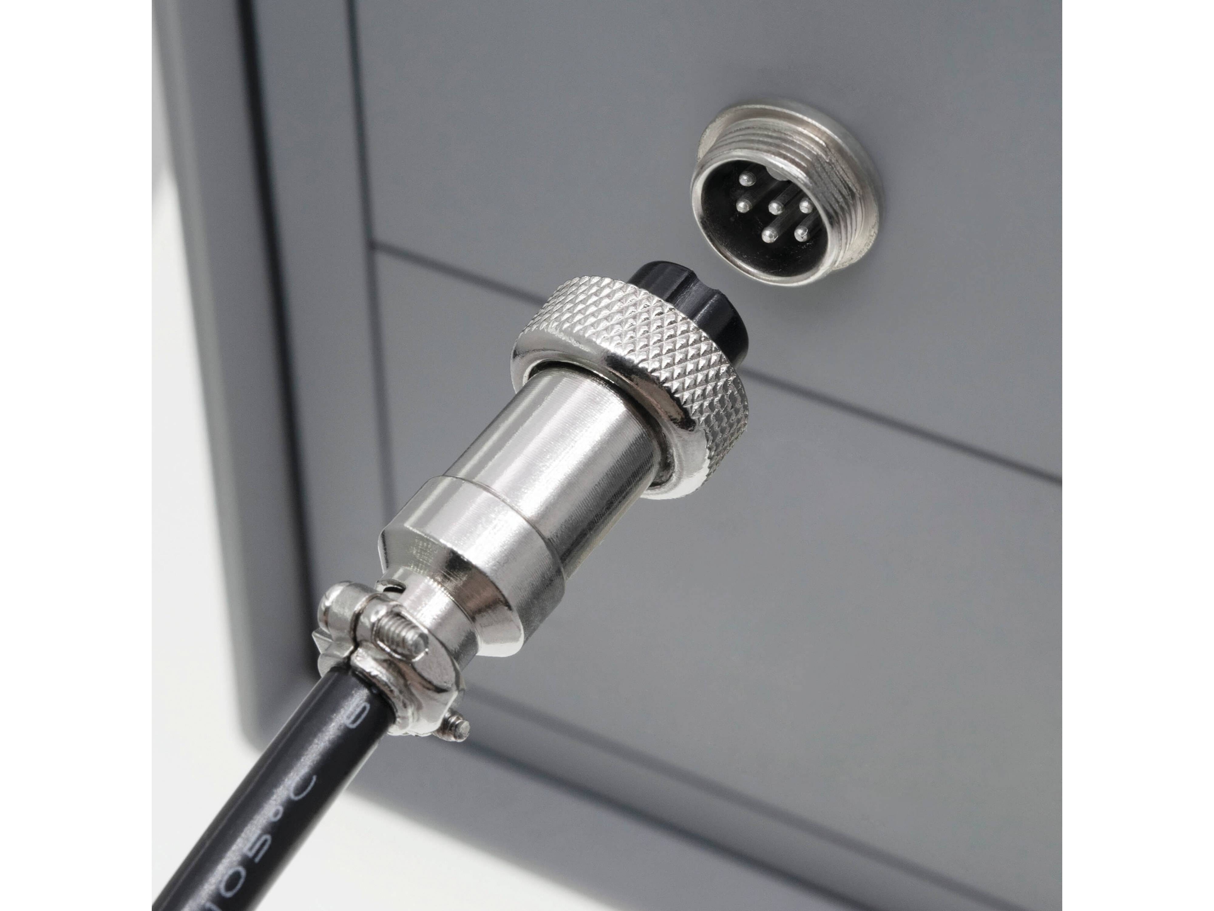 Ein metallischer Steckerverbinder ist teilweise in eine runde Multi-Pin-Buchse auf einem grauen Industriepanel eingesteckt und deutet auf eine elektrische Verbindung hin.
