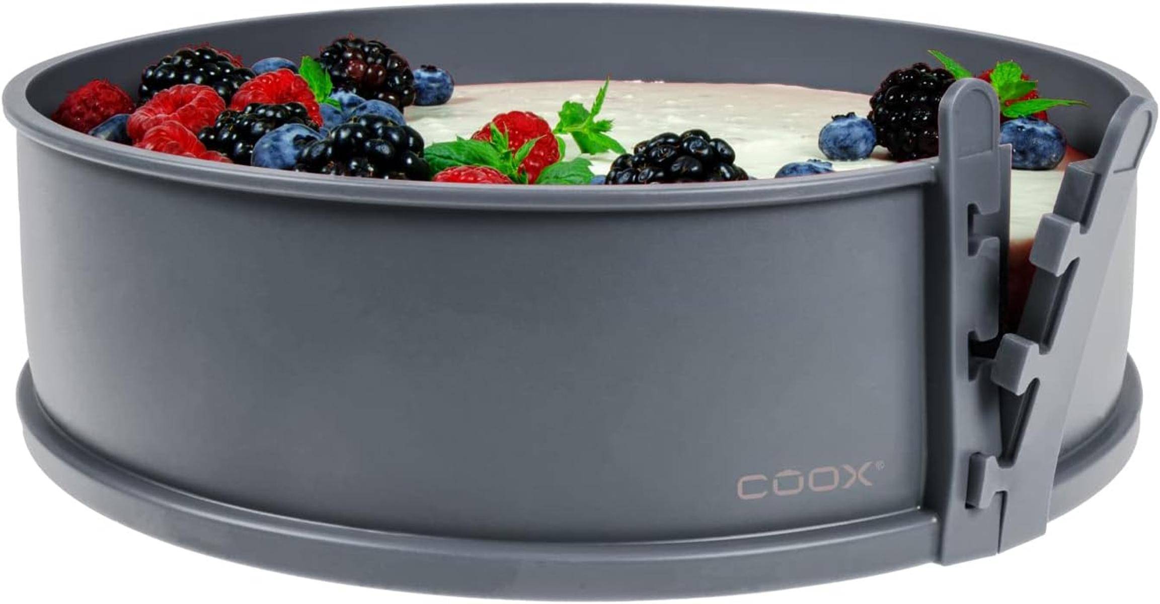 Eine runde graue Kuchenform gefüllt mit cremigem Nachtisch ist mit frischen Beeren belegt, darunter Blaubeeren, Erdbeeren und Himbeeren.