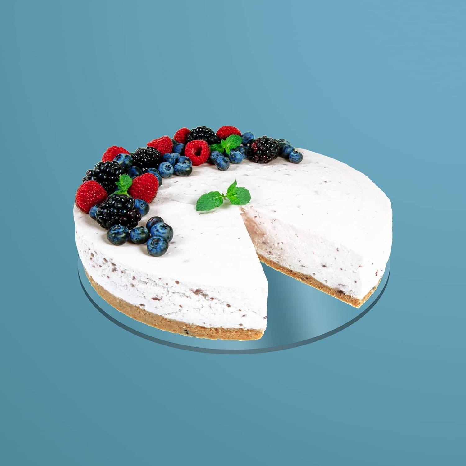 Ein Käsekuchen garniert mit Himbeeren, Brombeeren und Blaubeeren, belegt mit frischen Minzblättern, auf blauem Hintergrund.